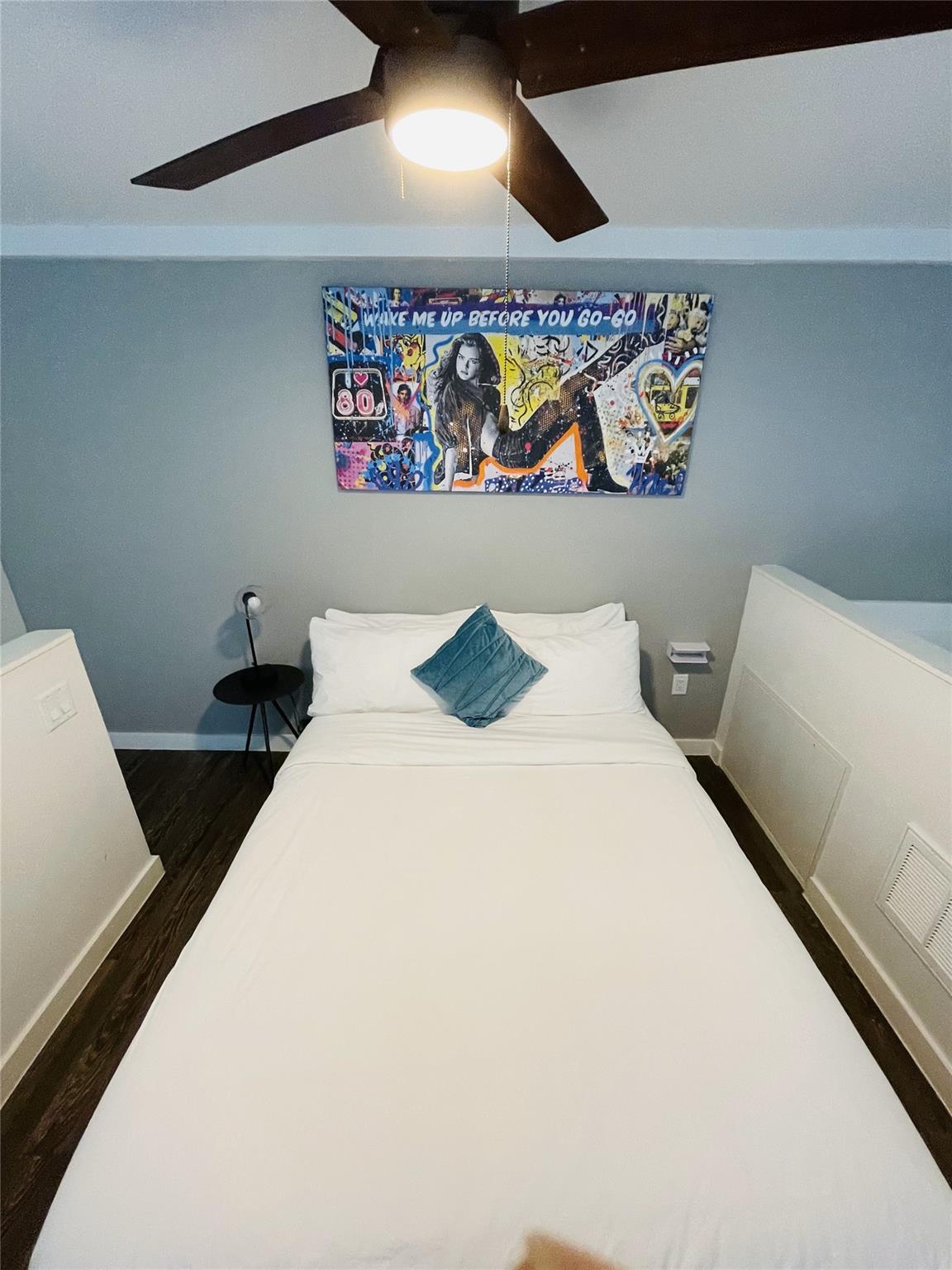Bedroom with a white bed, teal pillow, ceiling fan, and colorful music-themed wall art.