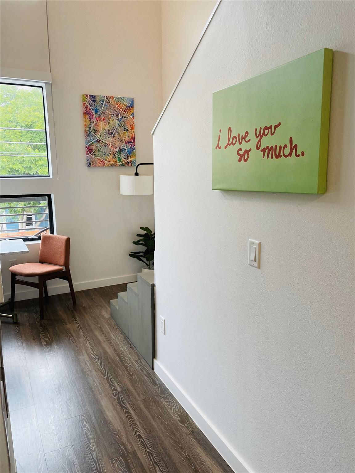 Interior landing with tall windows, a rust-colored chair, and a green “i love you so much” sign.