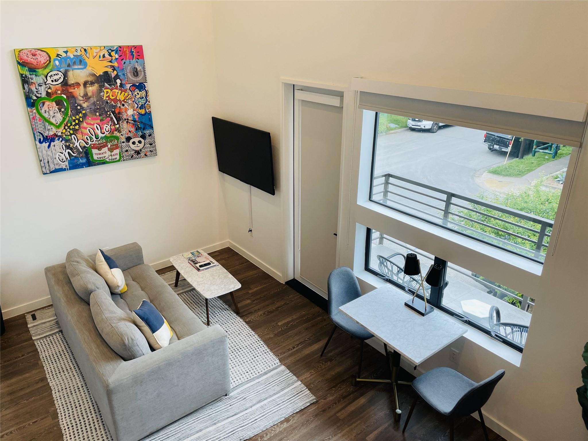 Furnished condo living and dining area with colorful wall art and tall balcony windows.