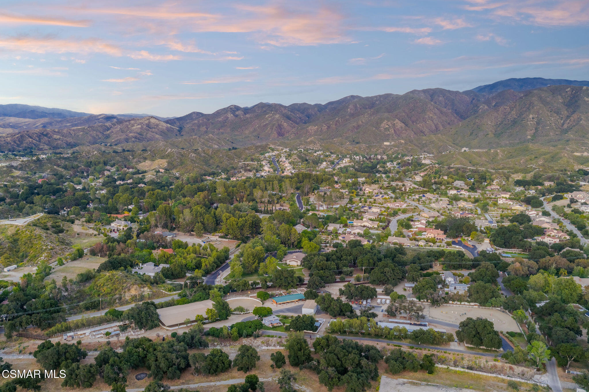 Aerial view of a hillside neighborhood with tree-lined roads and mountain ranges.