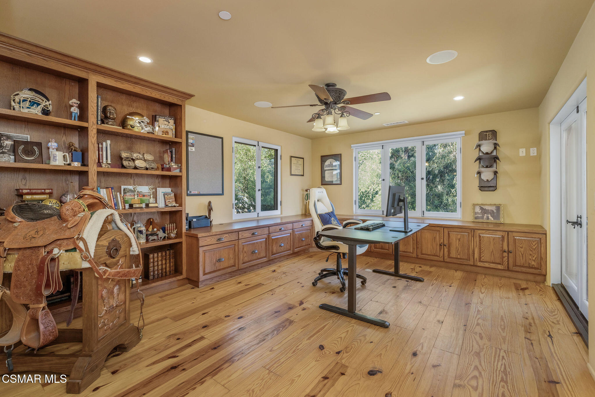Home office with built-in wood cabinetry, large windows, sports memorabilia, and Western saddles.