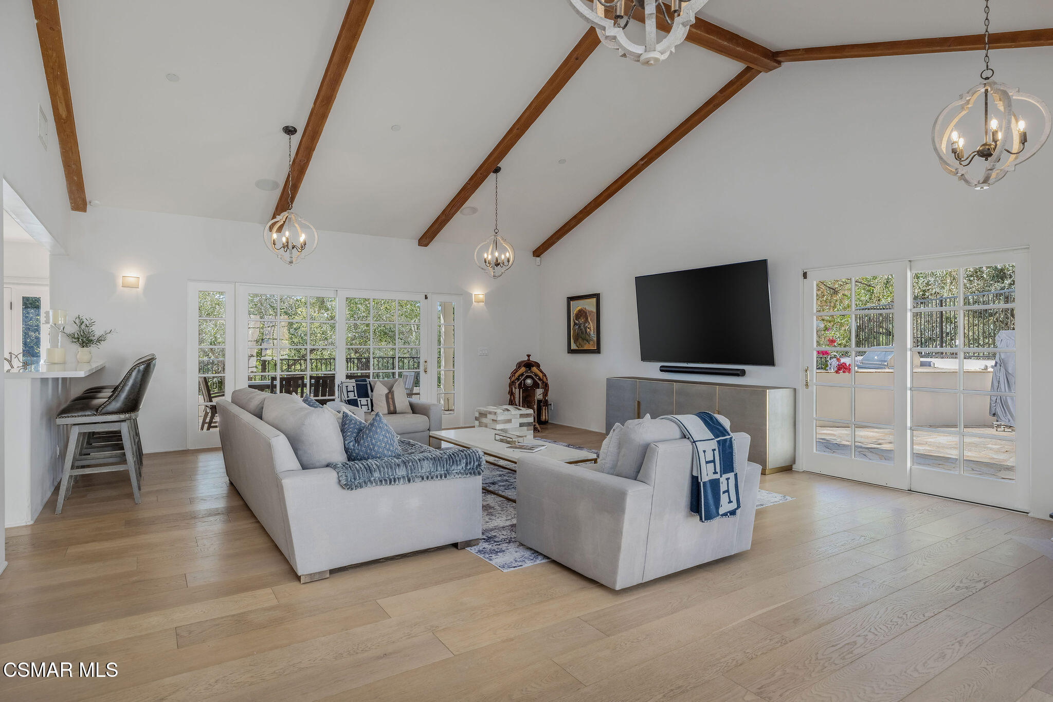 Living room with vaulted wood-beam ceiling, pale sofas, and French doors opening to a patio.