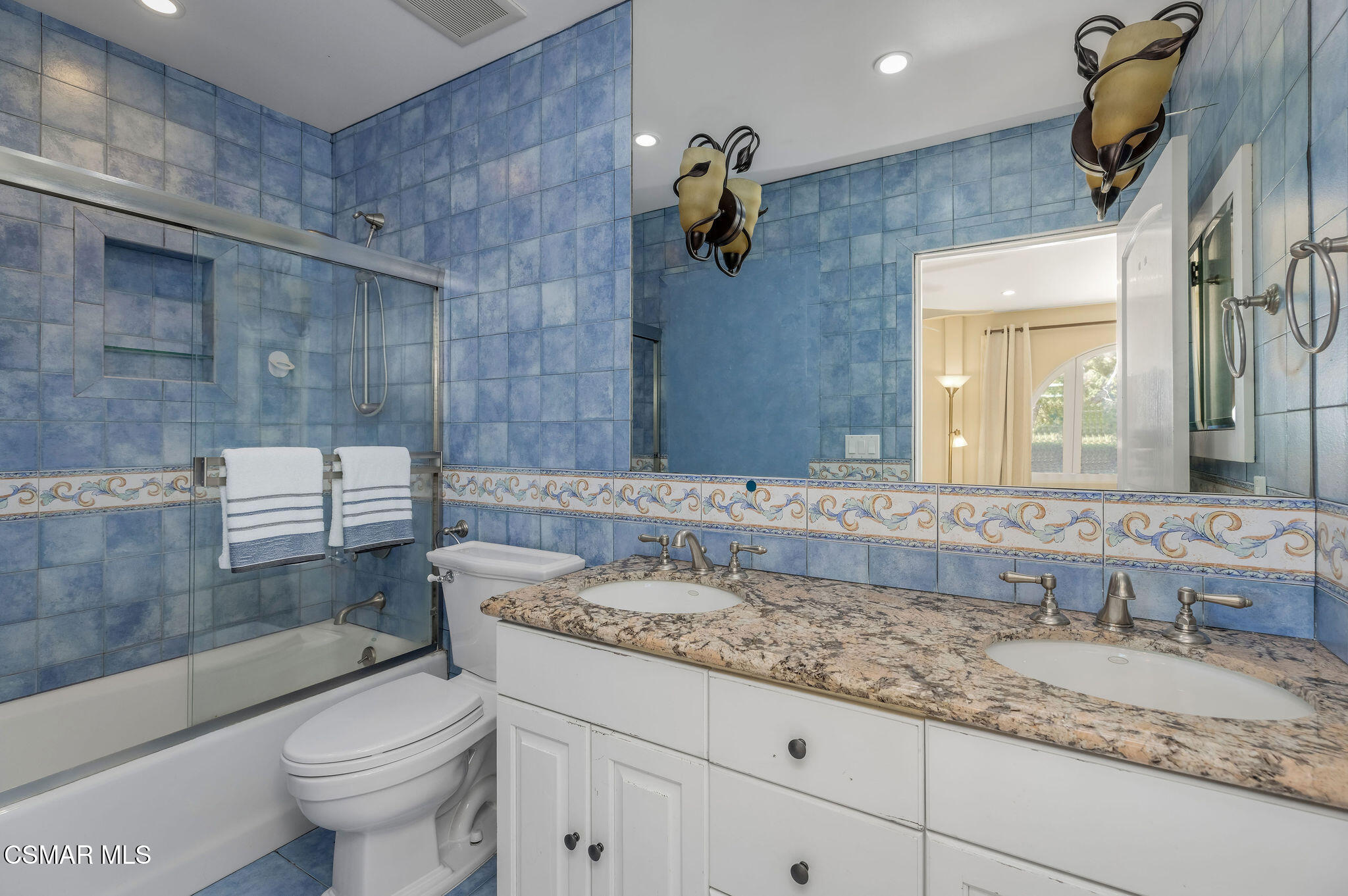 Bathroom with blue tile, glass-enclosed tub and shower, and a double-sink vanity.