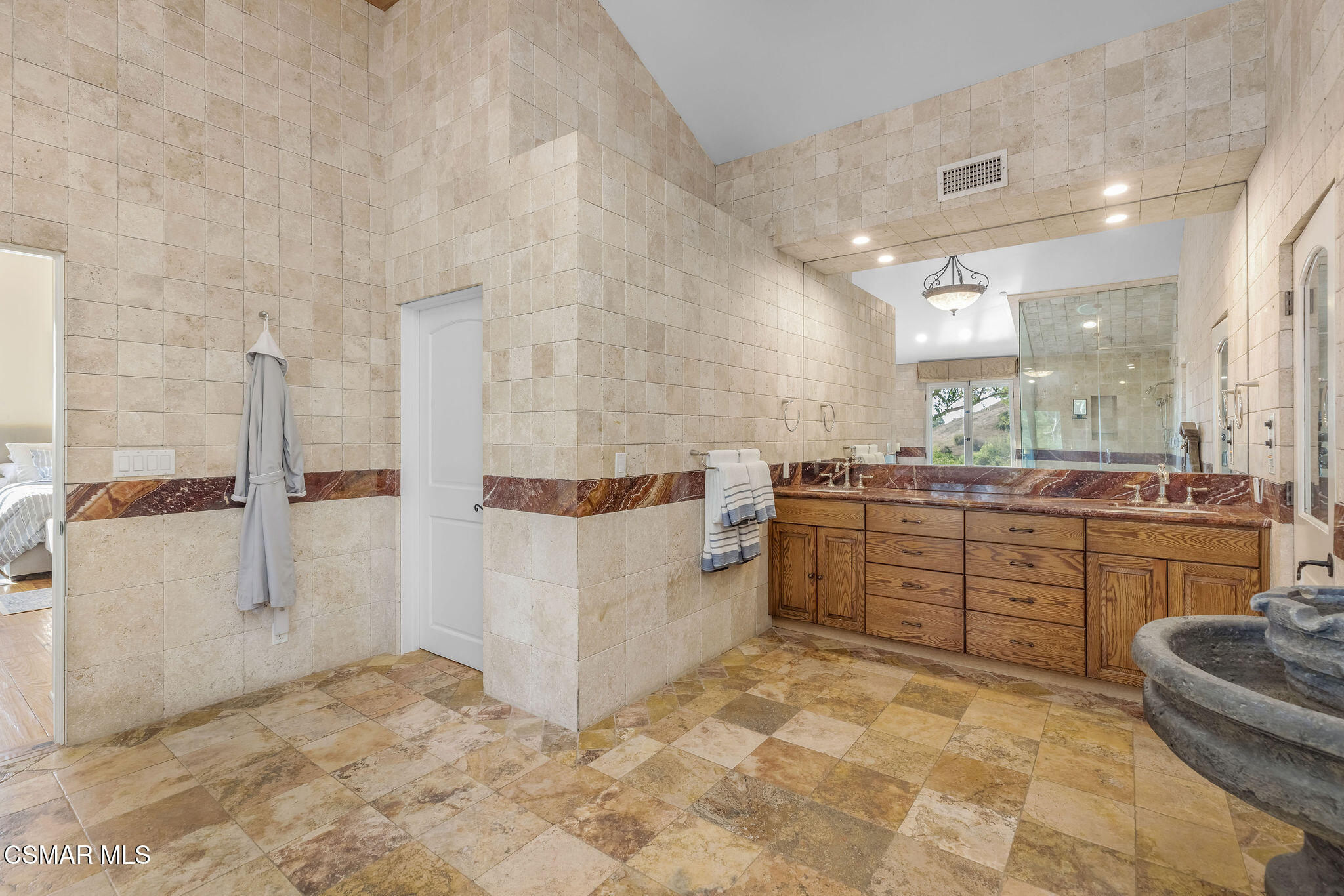Primary bathroom with a long wood double vanity, broad mirror, and glass shower.