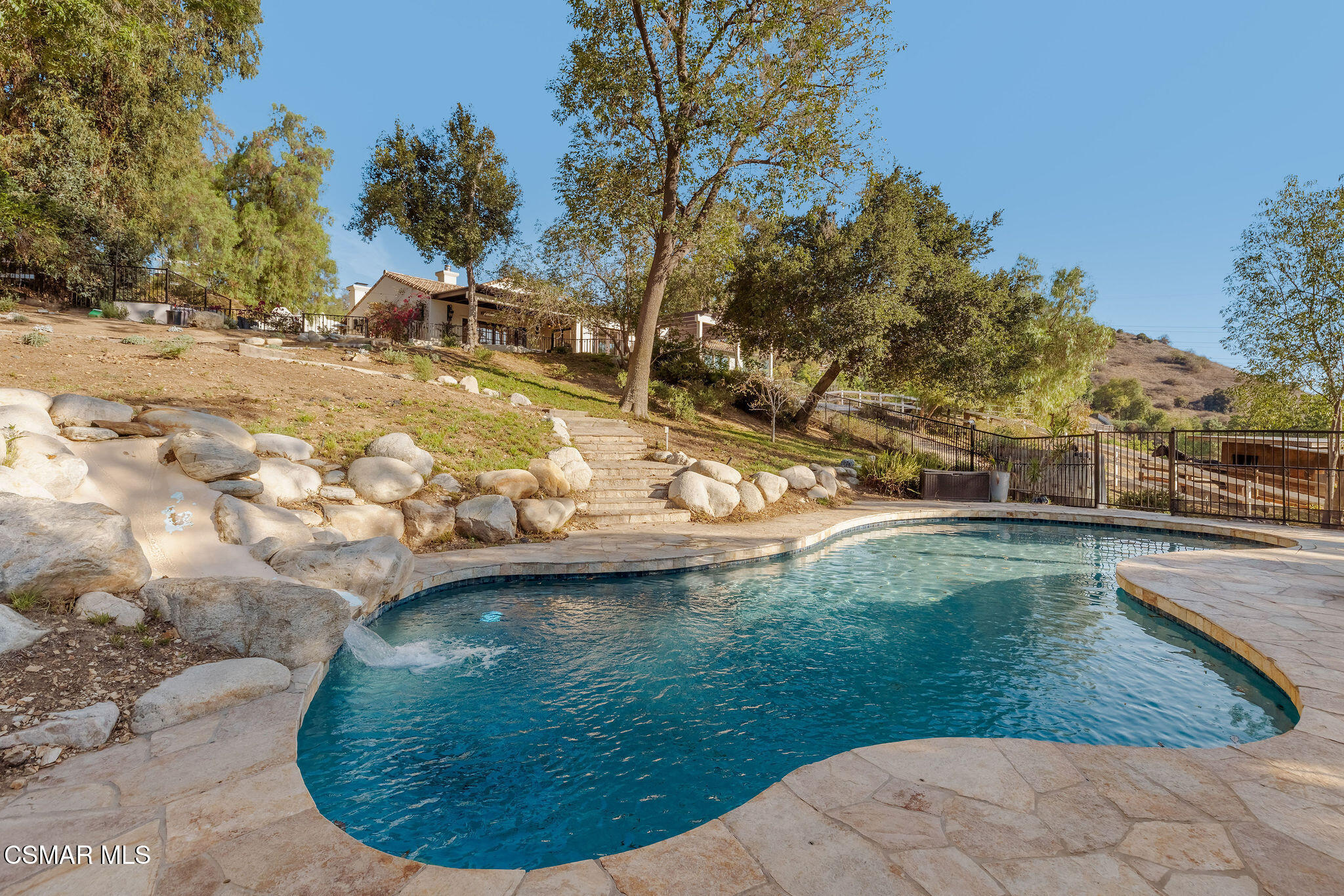Backyard swimming pool with a stone patio, rock waterfall, and hillside landscaping.