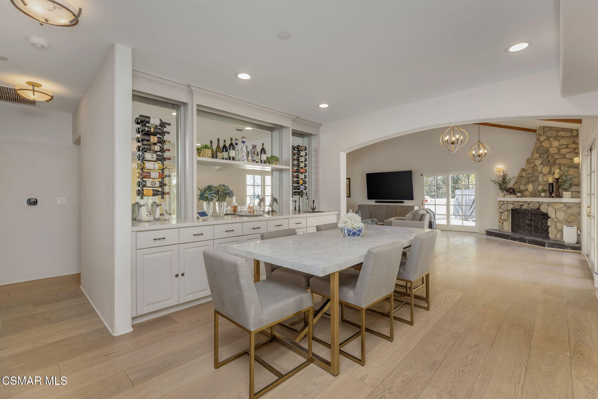 Dining room with marble table, built-in wine racks, and an arched opening to a stone-fireplace living room.