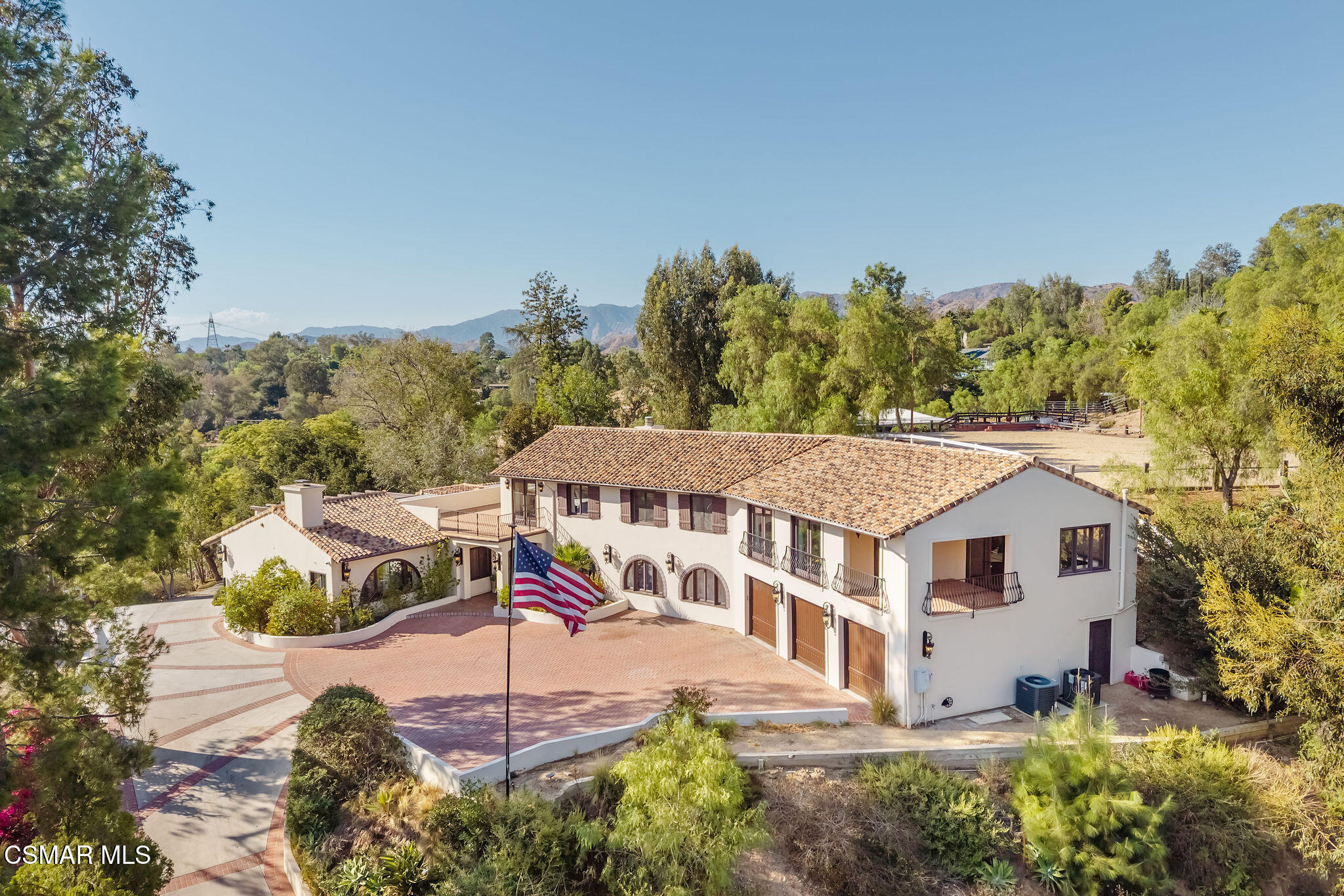 Aerial view of a two-story stucco home with tiled roofs, balconies, and a brick courtyard.
