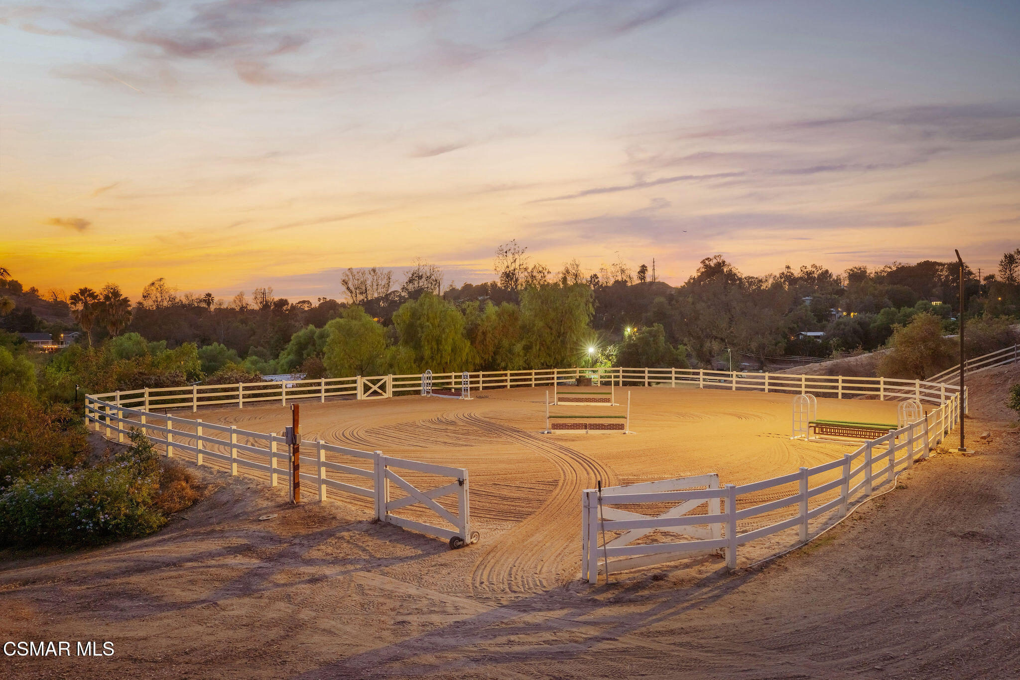 Outdoor riding arena with groomed sand and white fencing at sunset.