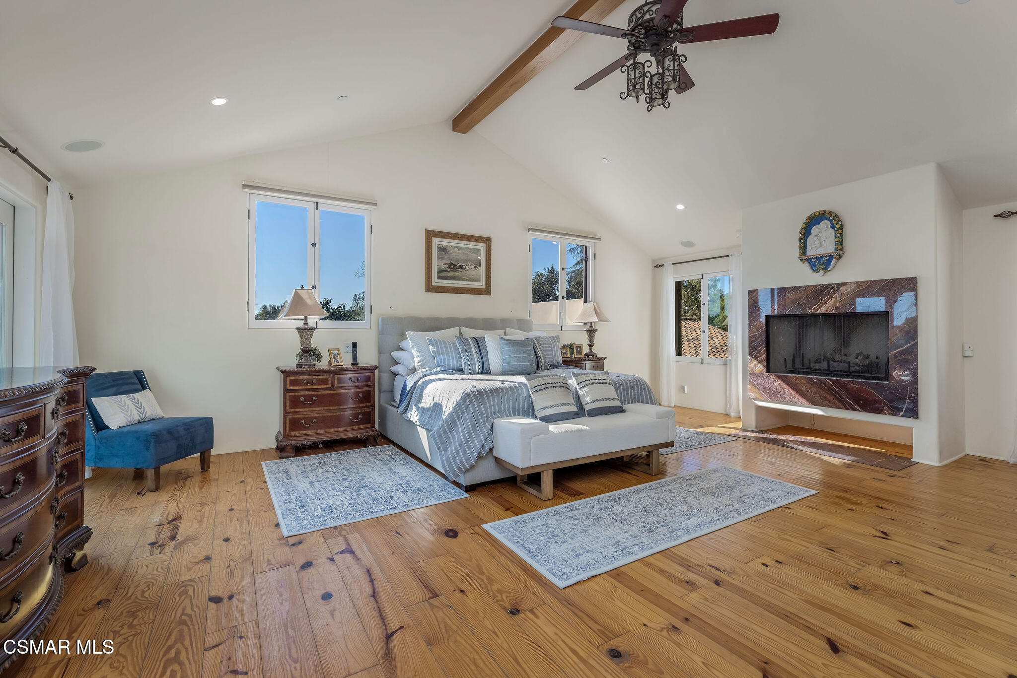 Furnished bedroom with vaulted ceiling, hardwood floors, and a large marble fireplace.