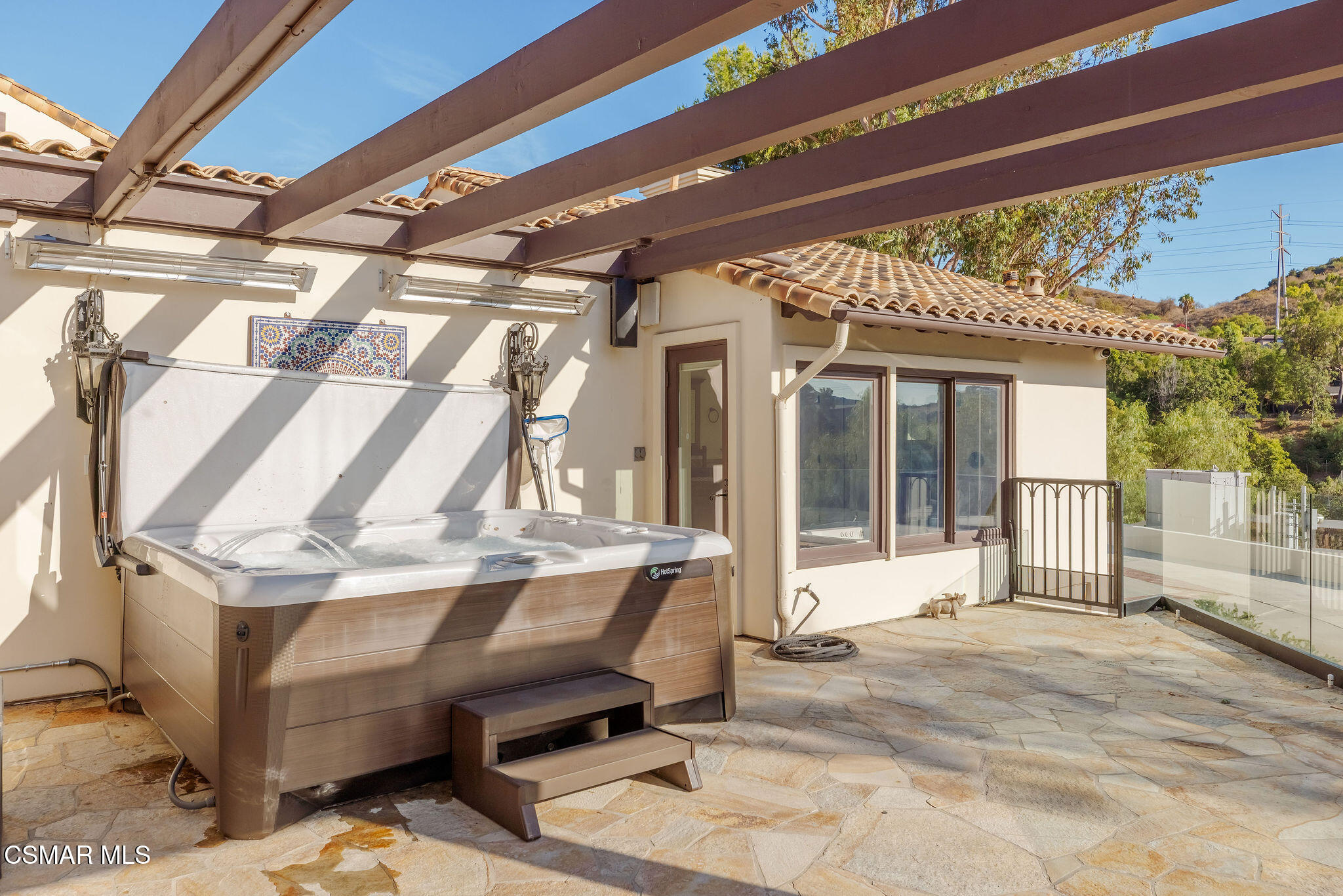 Back patio with a large hot tub beneath a wood pergola and a glass railing.