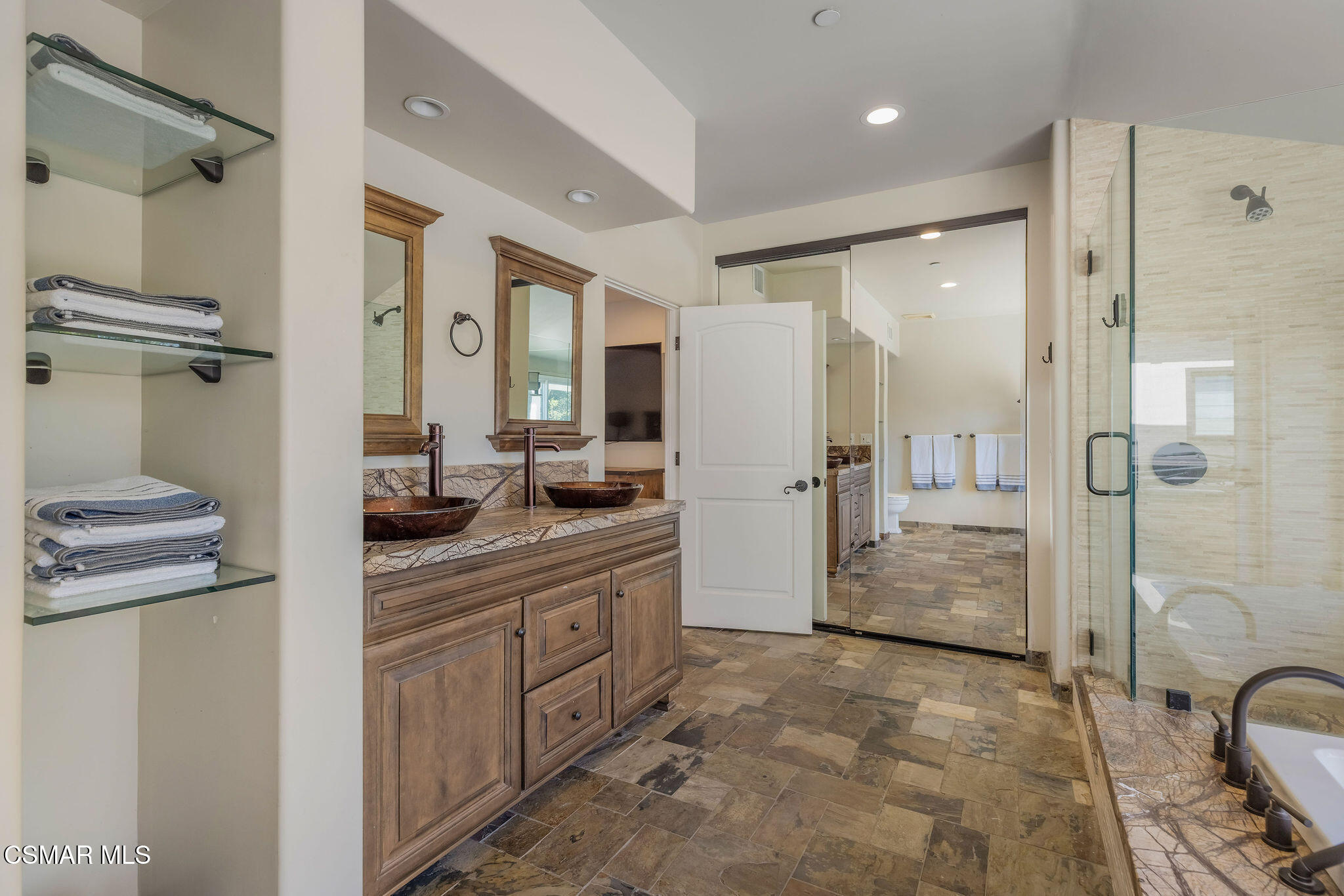 Bathroom with a double wood vanity, vessel shower, and stone tile flooring.