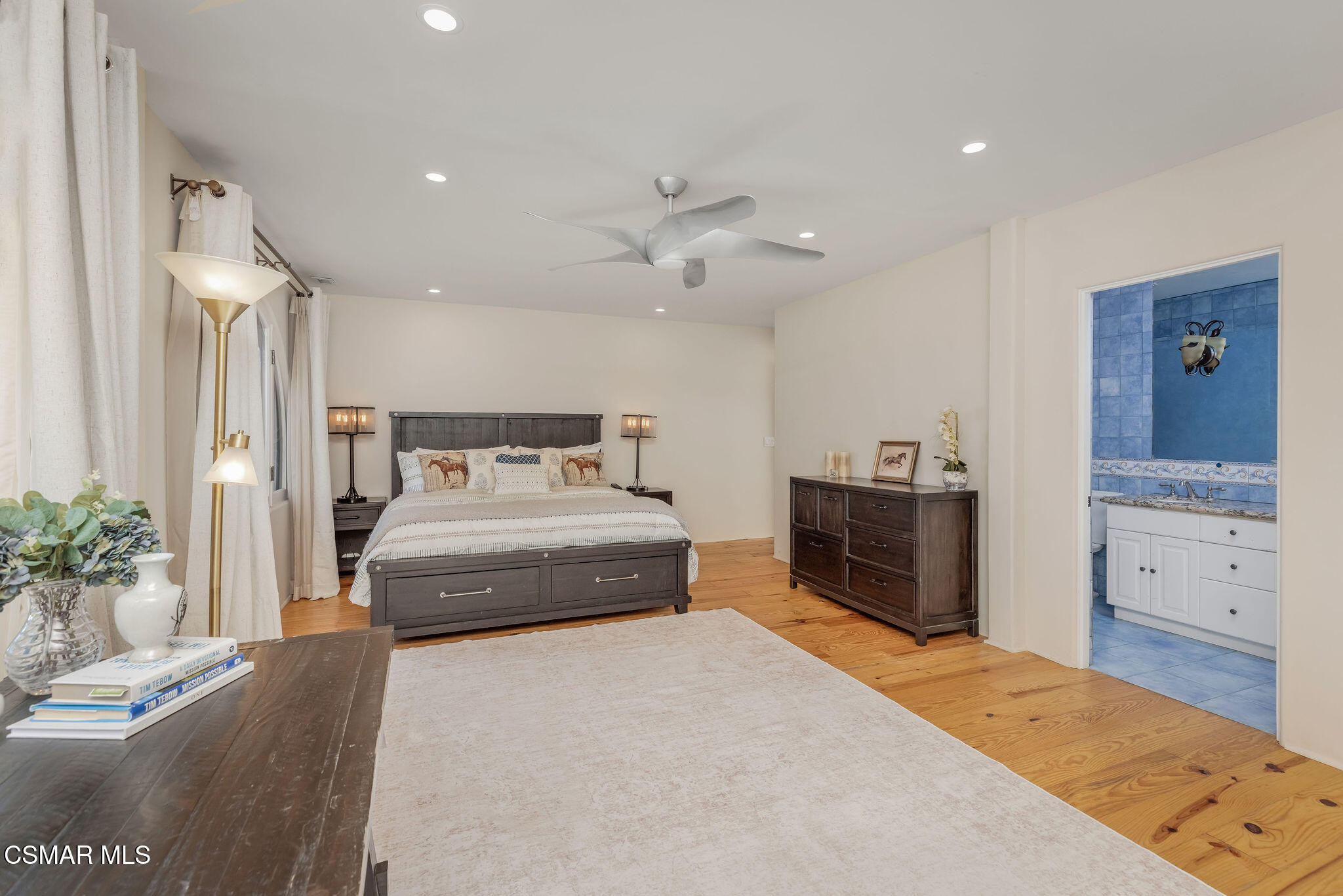 Furnished bedroom with a dark wood bed, hardwood floors, ceiling fan, and adjoining blue-tiled bathroom.