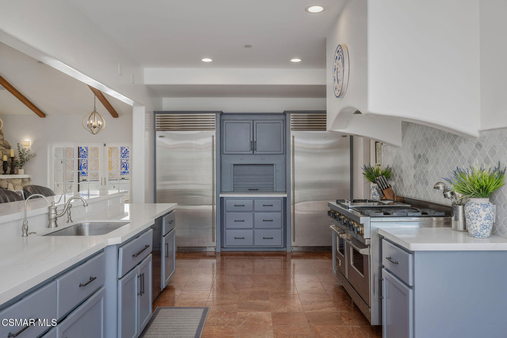 Kitchen with blue-gray cabinets, two stainless refrigerators, a large range, and white counters.