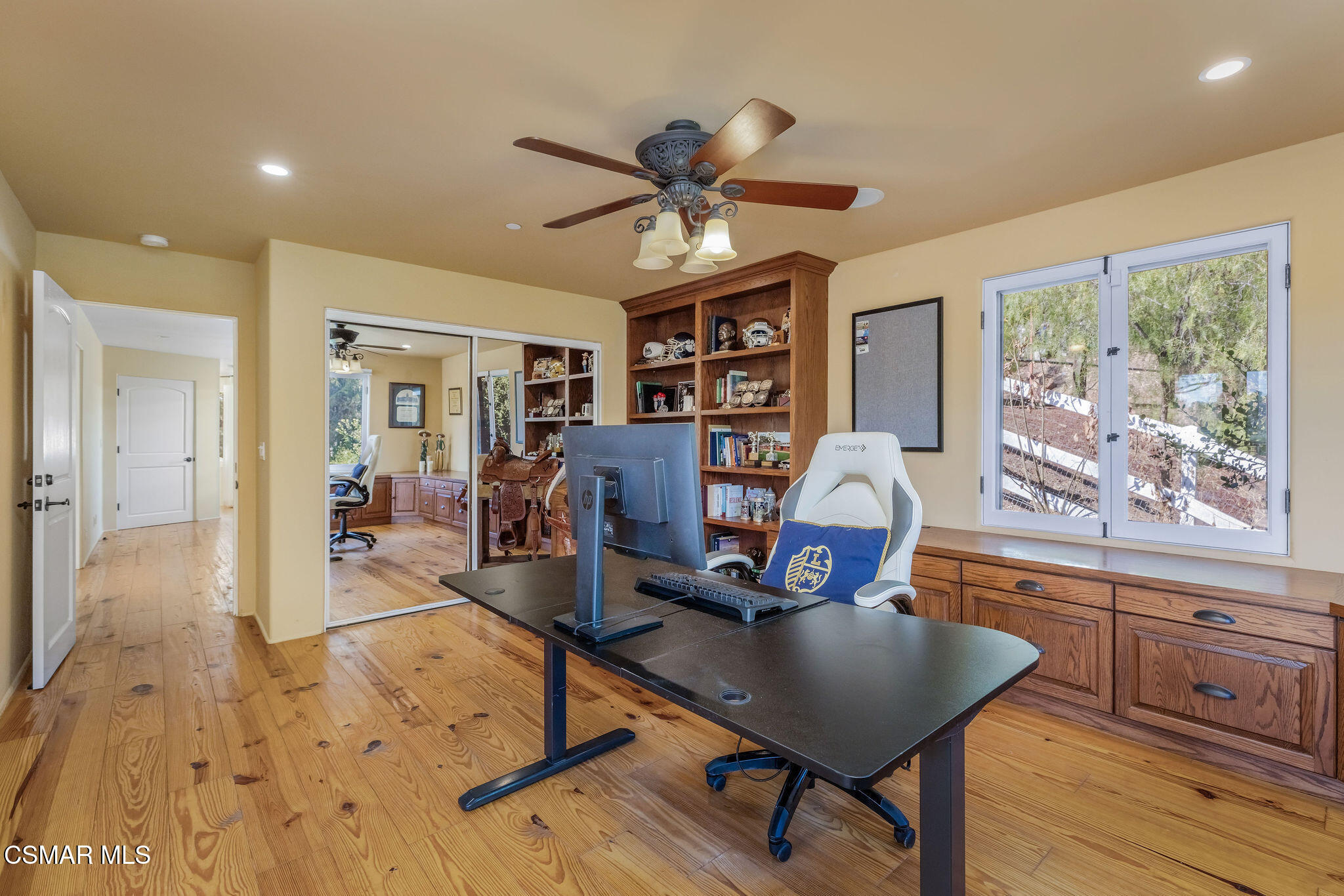 Home office with a black desk, built-in wood shelving, and a window overlooking trees.