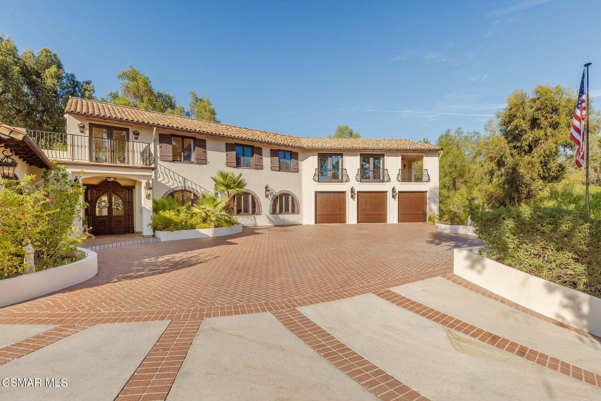 Two-story stucco home with terracotta roof, arched windows, balconies, and a broad brick driveway.