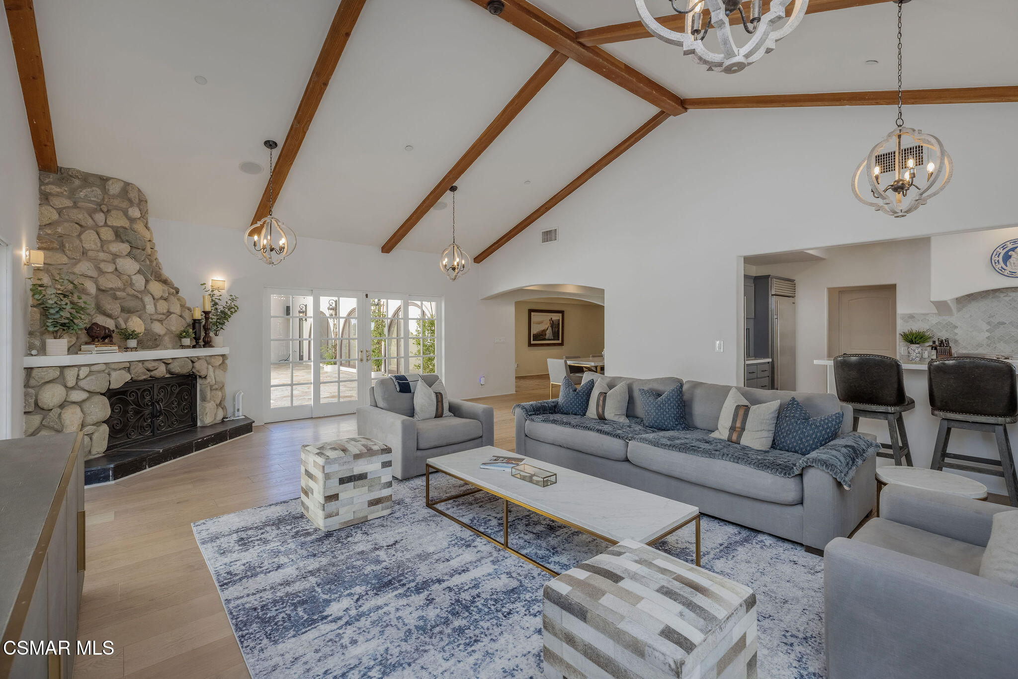 Living room with a stone fireplace, vaulted wood-beam ceiling, gray sofas, and French doors.