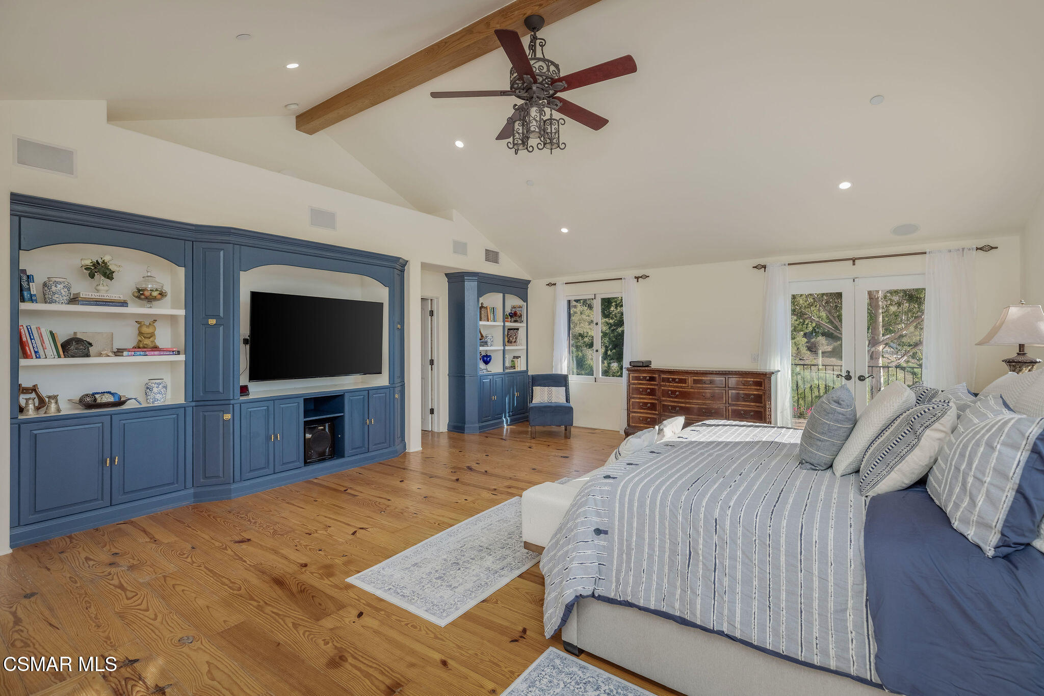 Bedroom with blue built-ins, a vaulted ceiling, and French doors overlooking trees.