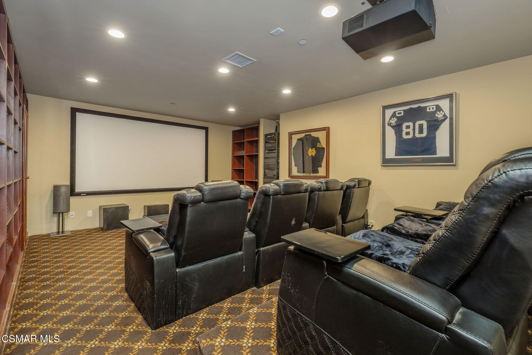 Home theater with black leather recliners facing a large screen and framed sports jerseys.