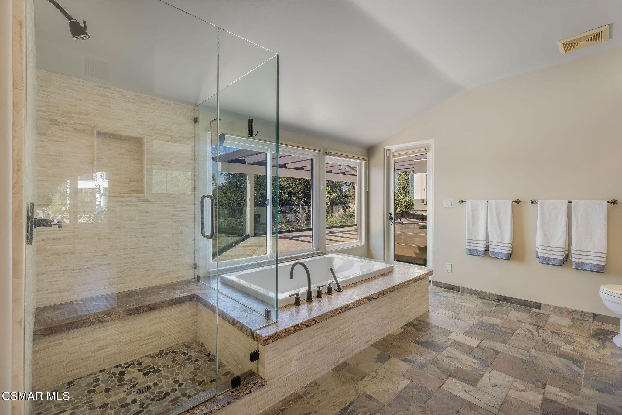 Spacious bathroom with a glass walk-in shower, raised soaking tub, and windows facing a patio.