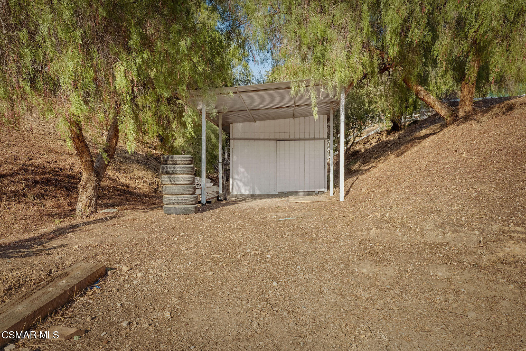 Open-sided metal shelter on a wooded hillside, with a stack of tires beside it.