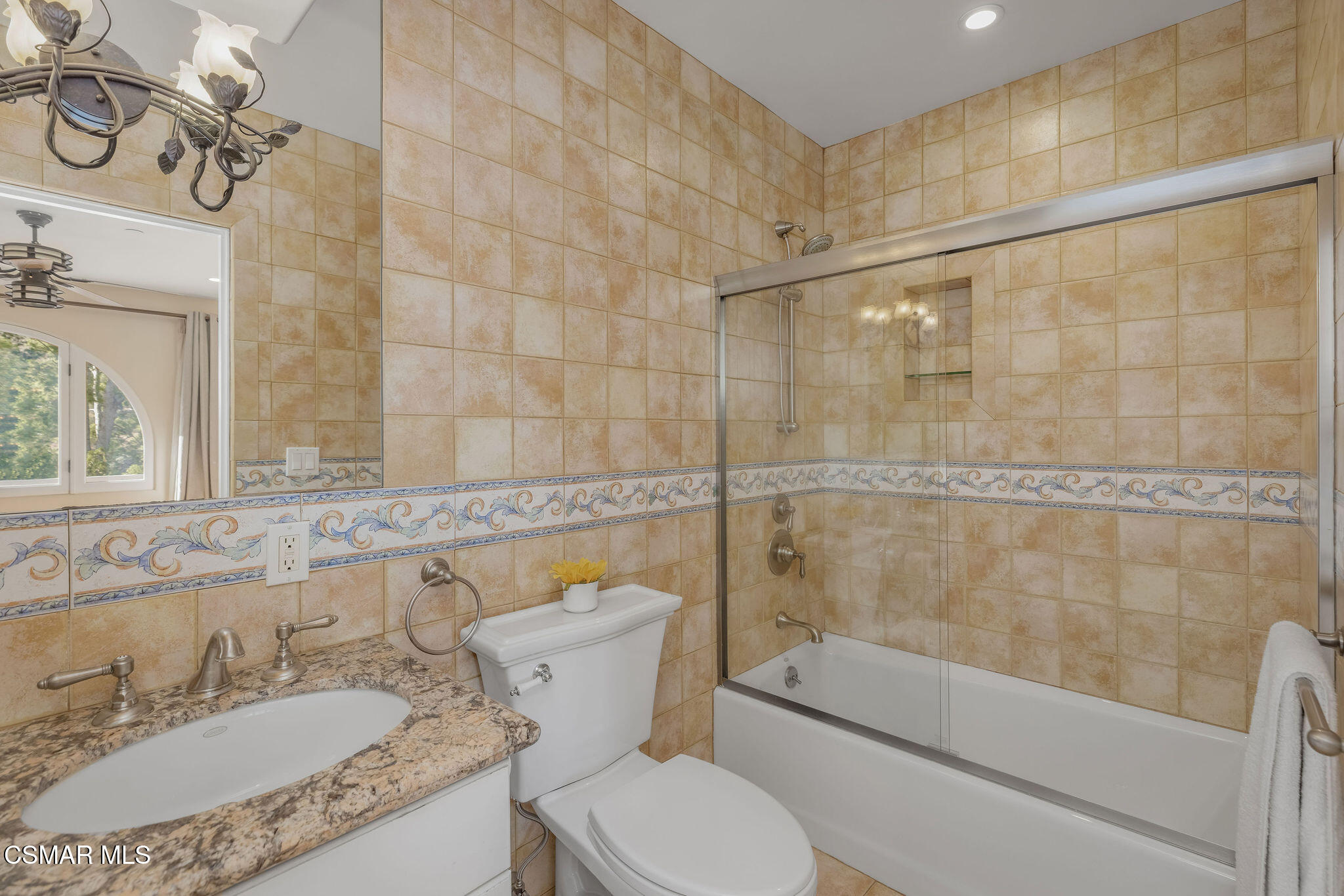 Bathroom with tan tiled walls, granite vanity, and glass-enclosed bathtub and shower.