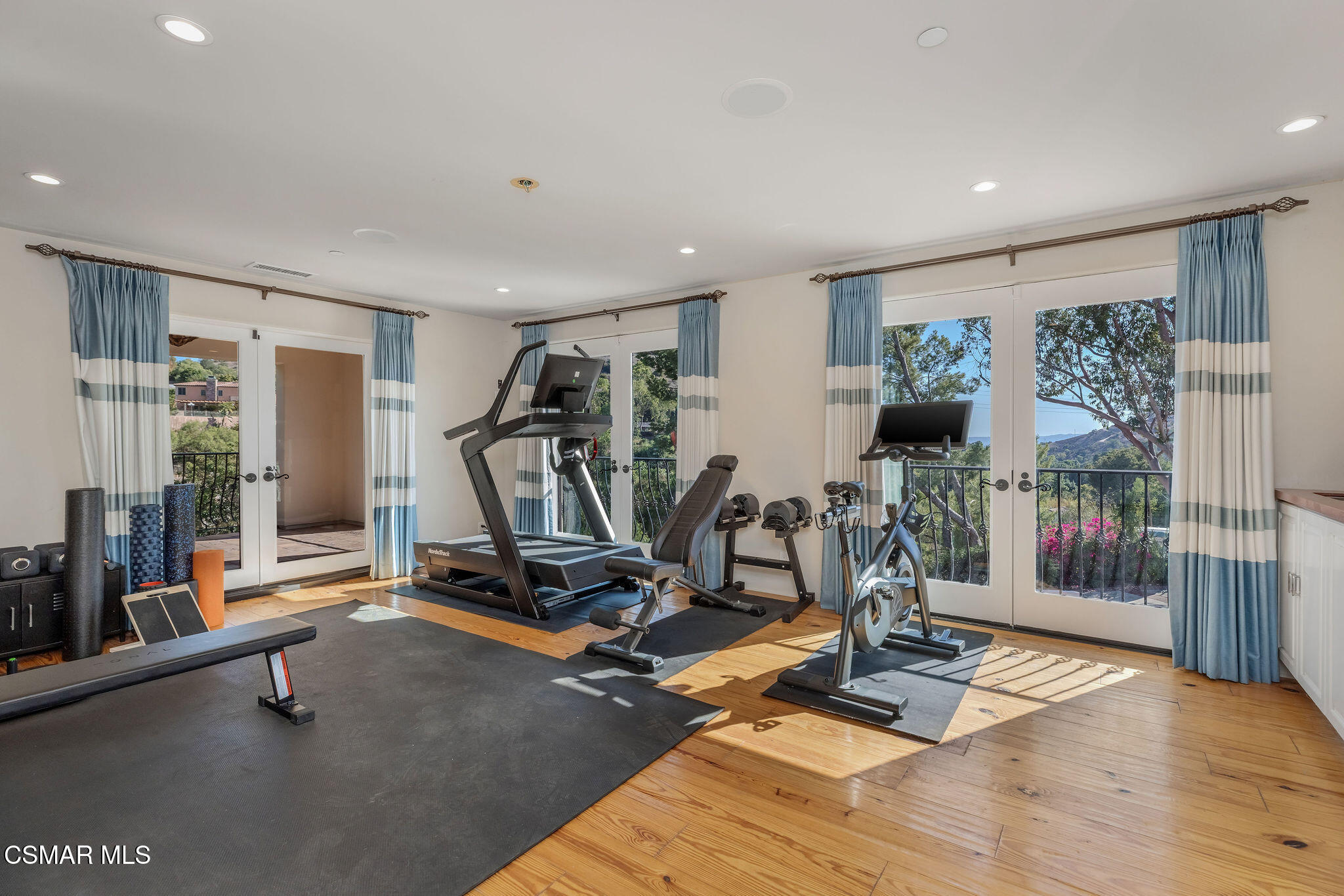 Home gym with treadmill and stationary bike beside glass doors overlooking green hills.