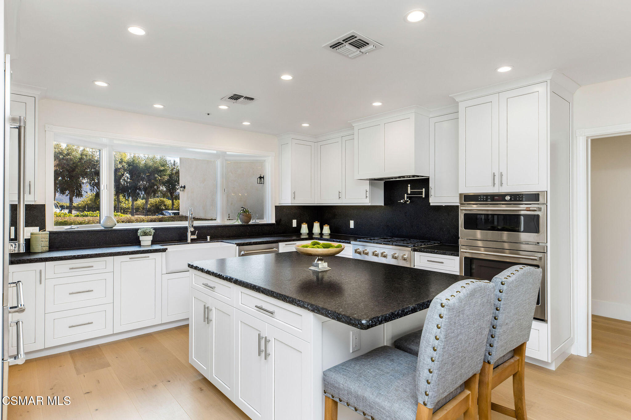 Bright kitchen with white cabinets, dark countertops, a large island, and windows overlooking trees.