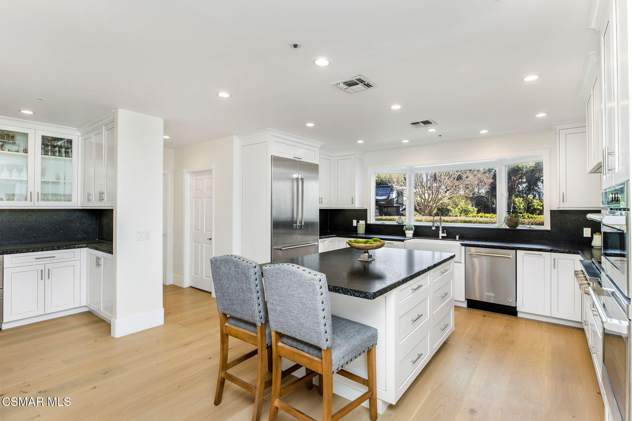 Bright white kitchen with a large dark-counter island, two gray stools, and stainless steel appliances.