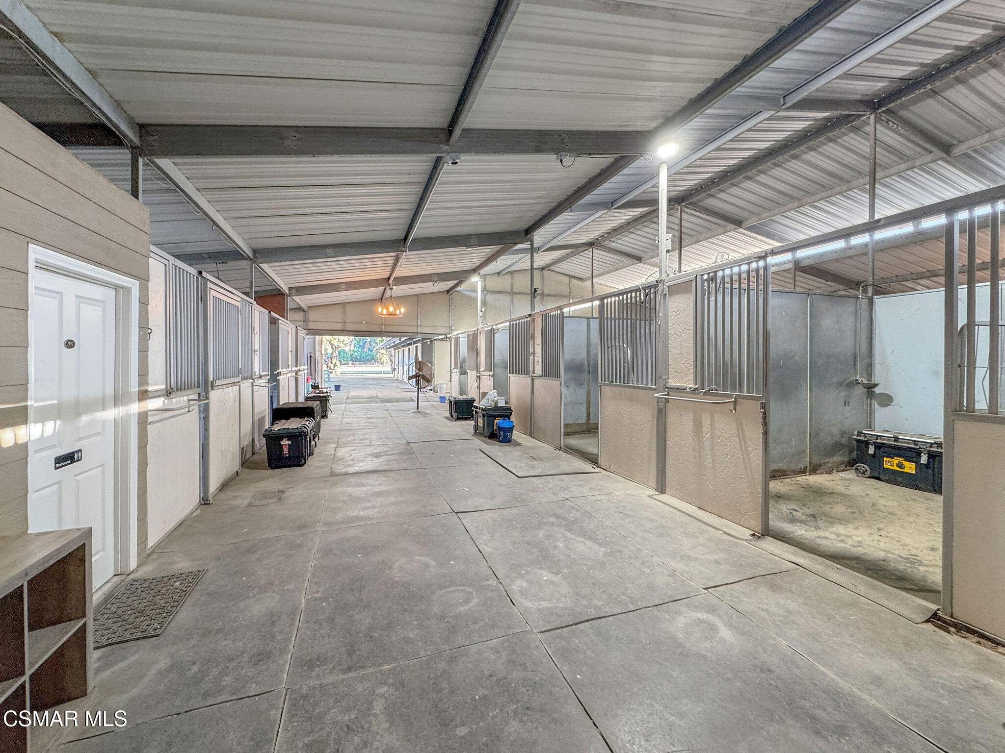 Covered horse stable aisle lined with metal stalls and concrete flooring.
