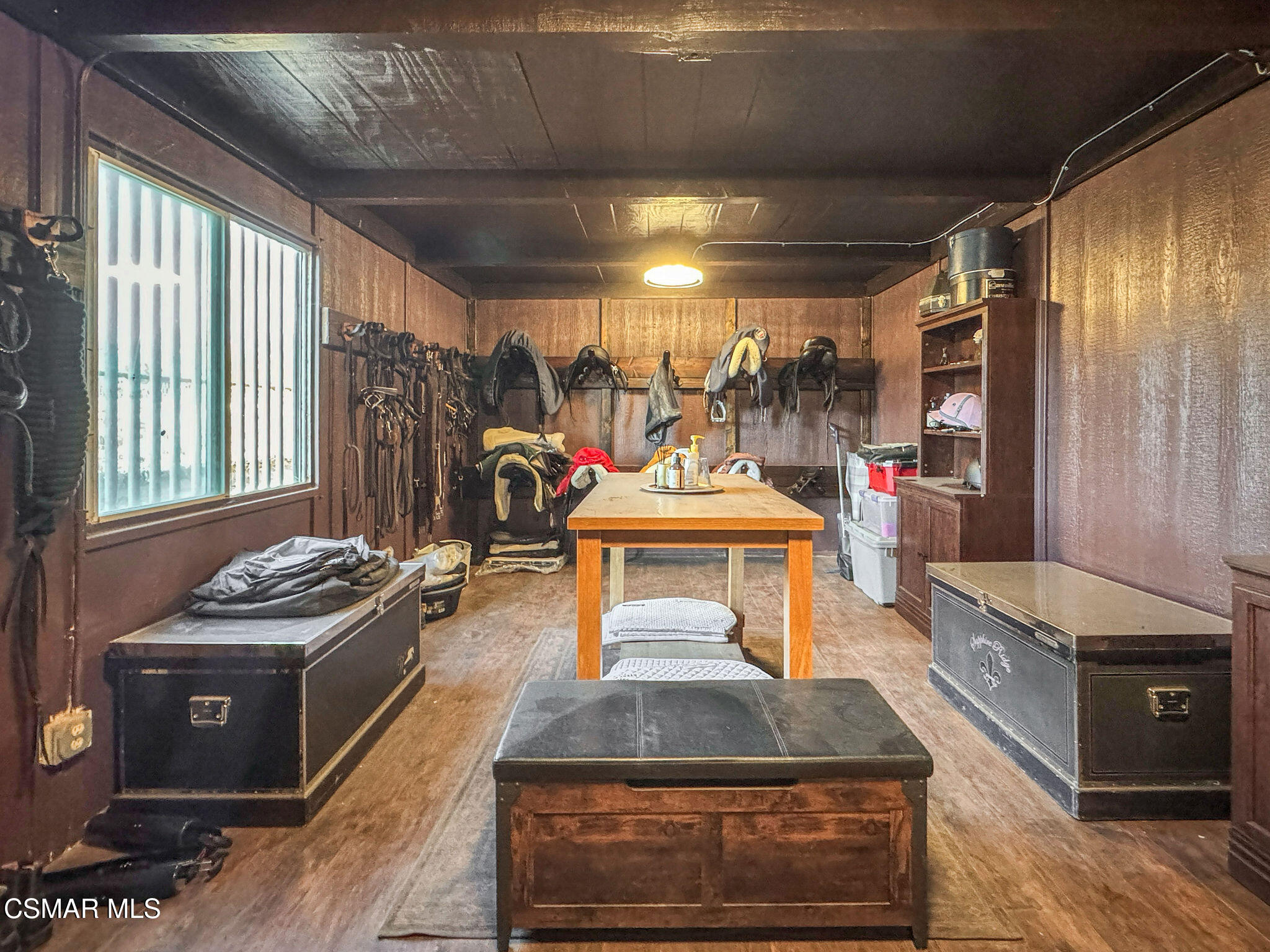 Tack room with saddles and bridles on the walls and a central worktable.