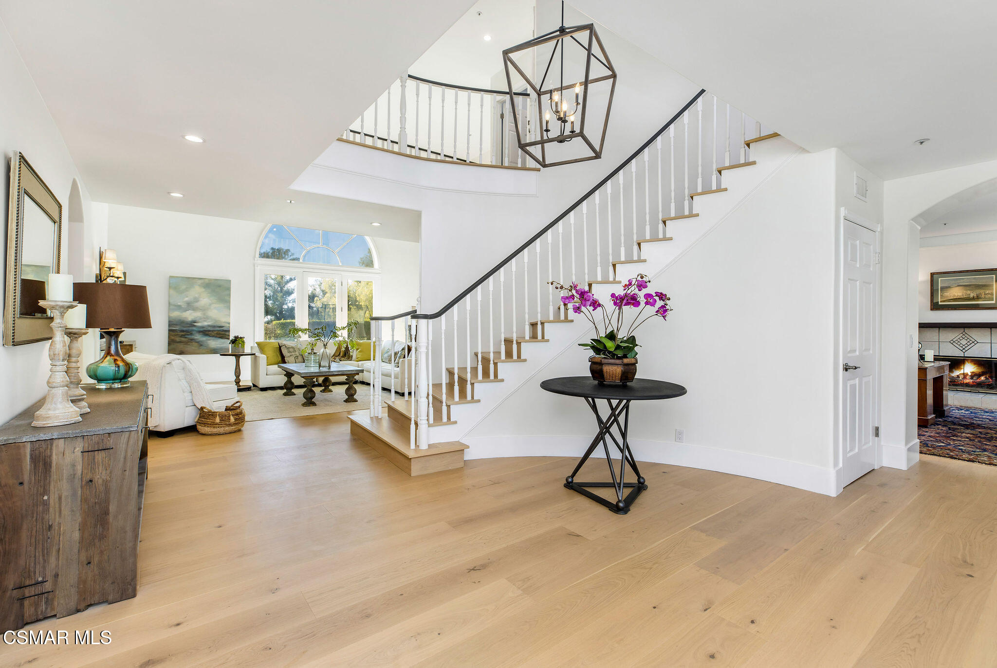 Furnished entryway with a white staircase, geometric chandelier, and sitting area beneath an arched window.