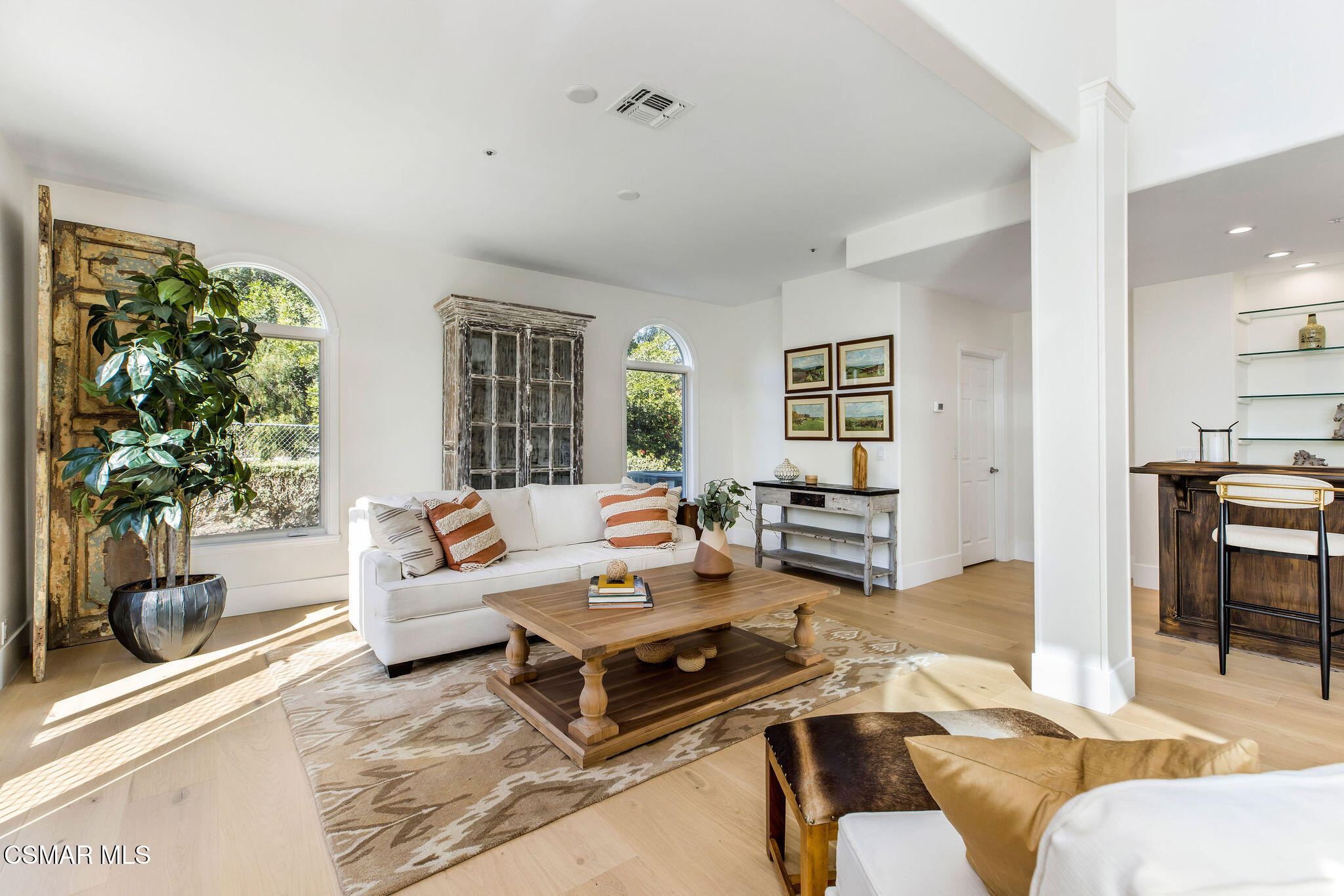 Furnished living room with arched windows, white sofas, and a rustic wood coffee table.