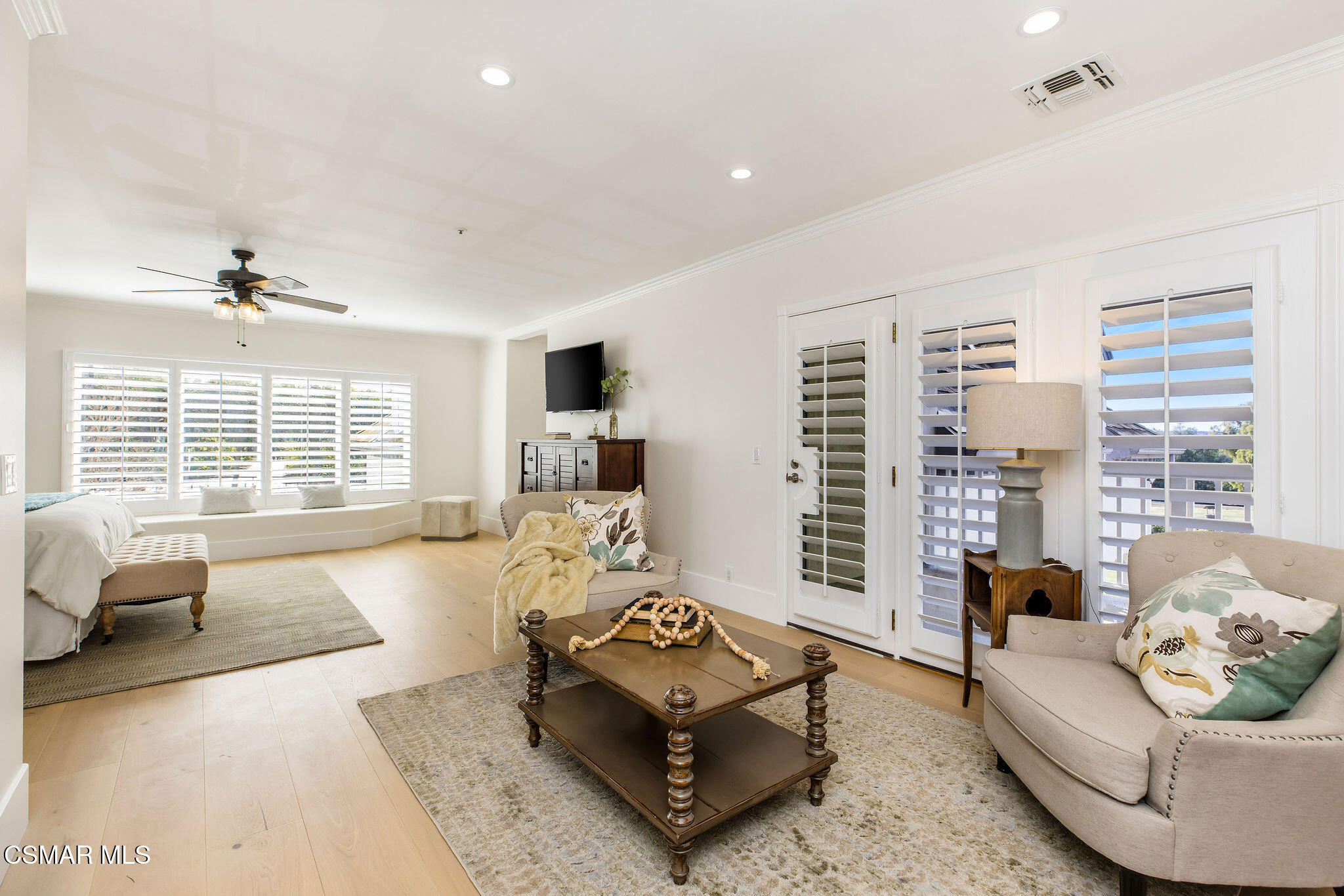Bedroom and sitting area with plantation shutters, upholstered seating, and a wood coffee table.
