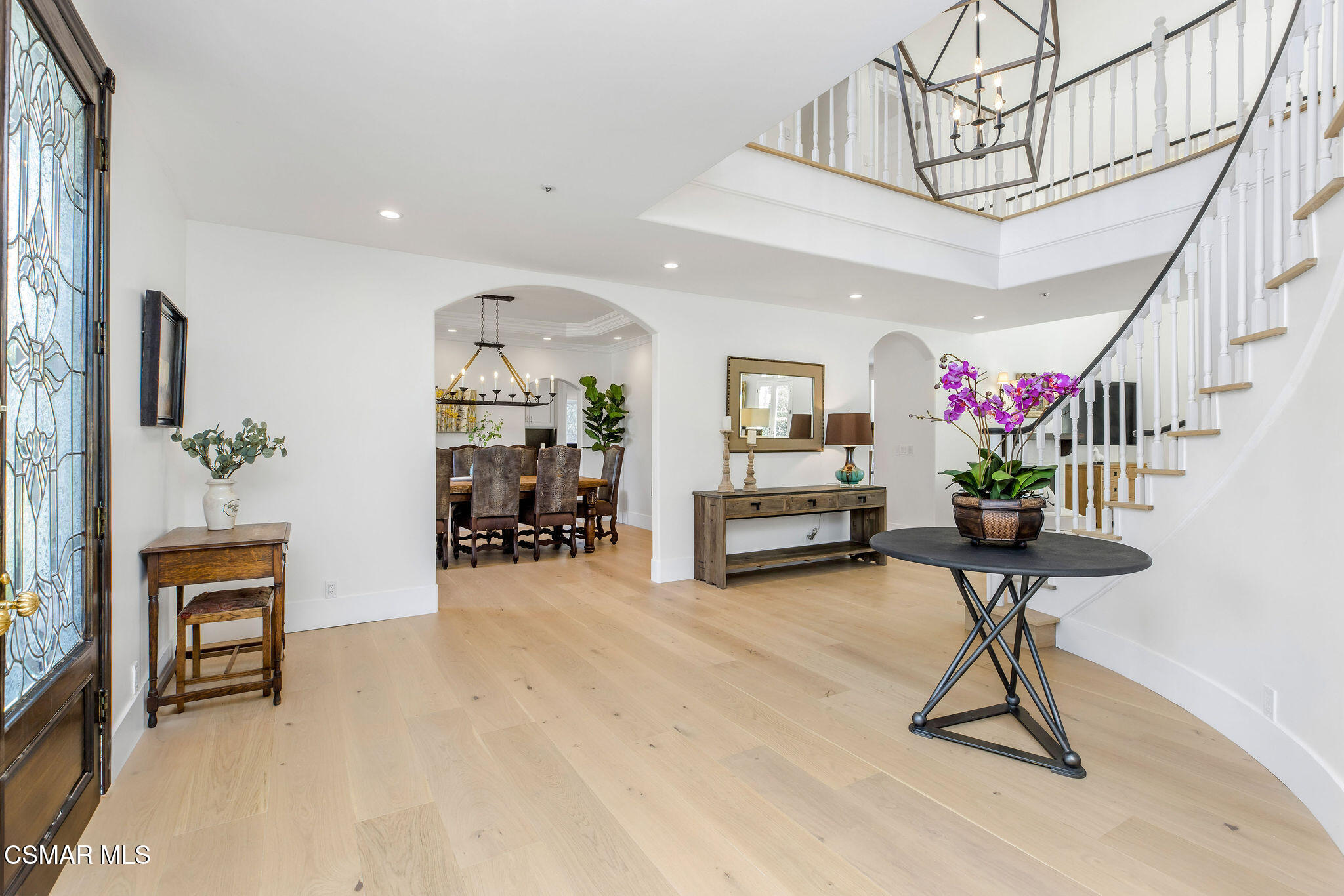 Furnished entryway with a glass front door, open staircase, and dining room beyond.