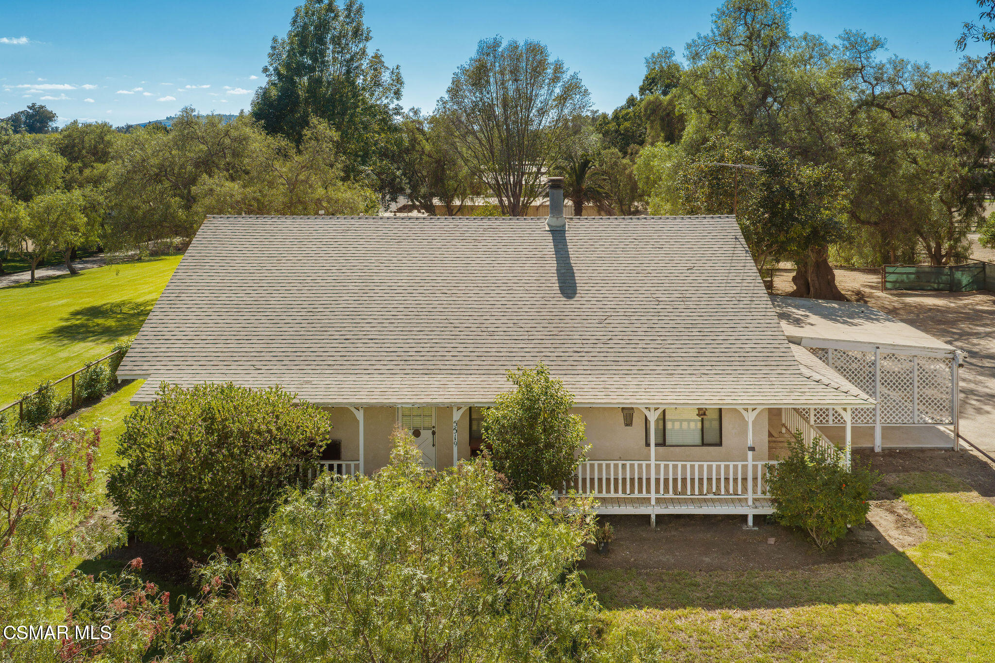 Single-story home with a broad shingled roof, covered porch, and mature trees around the lawn.