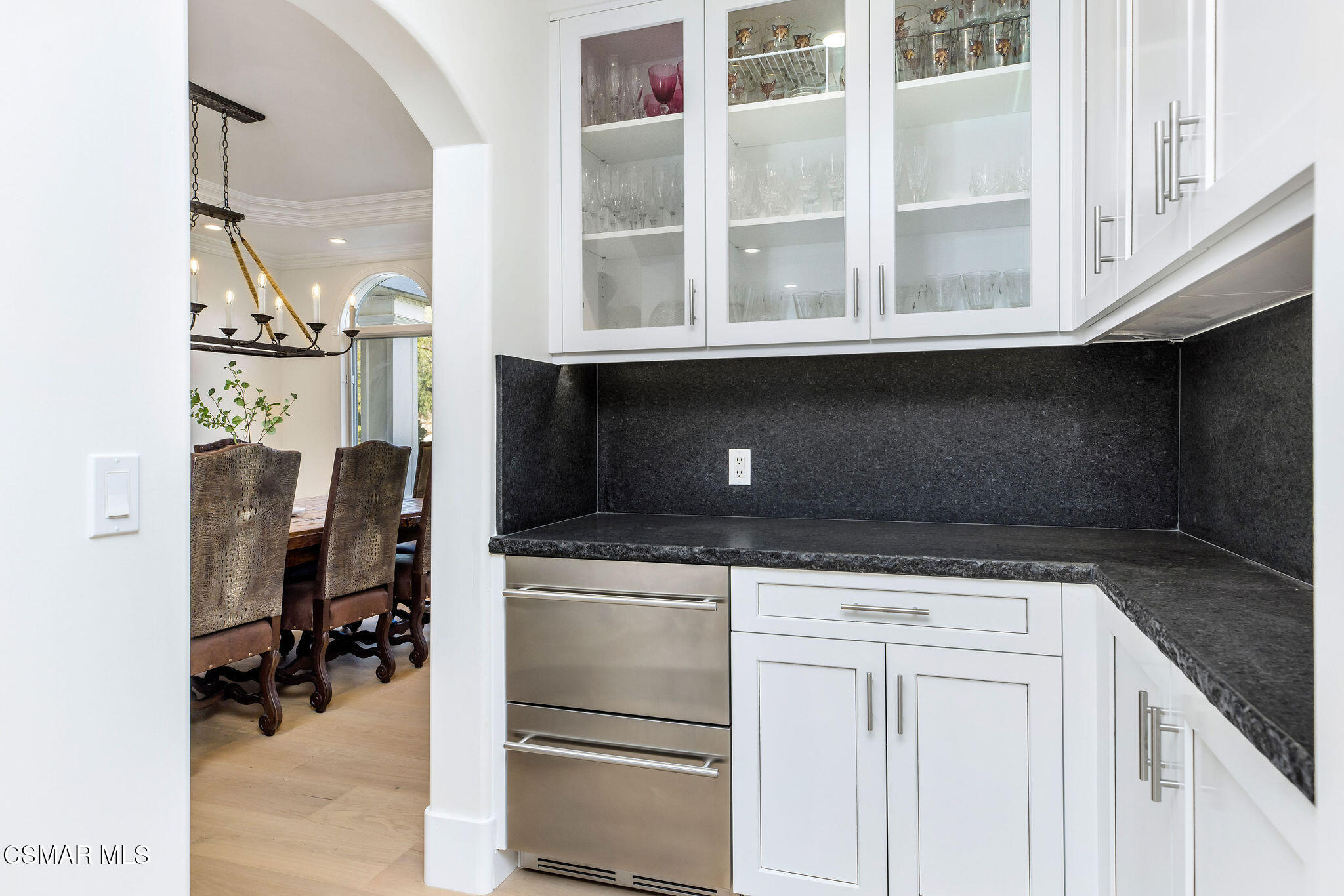 Kitchen with glass-front cabinets, dark stone counters, and an arched opening to the dining room.