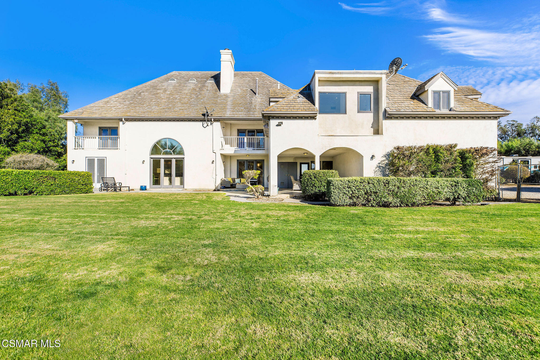 Rear of a two-story cream home with arched patio, balconies, and broad green lawn.
