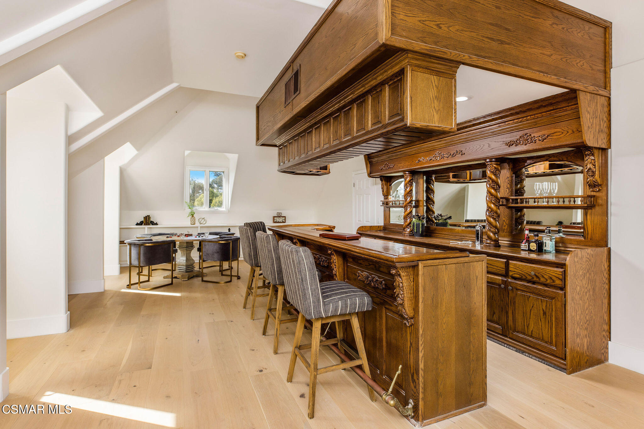 Interior bar with ornate dark wood cabinetry and upholstered stools beside a small dining table.