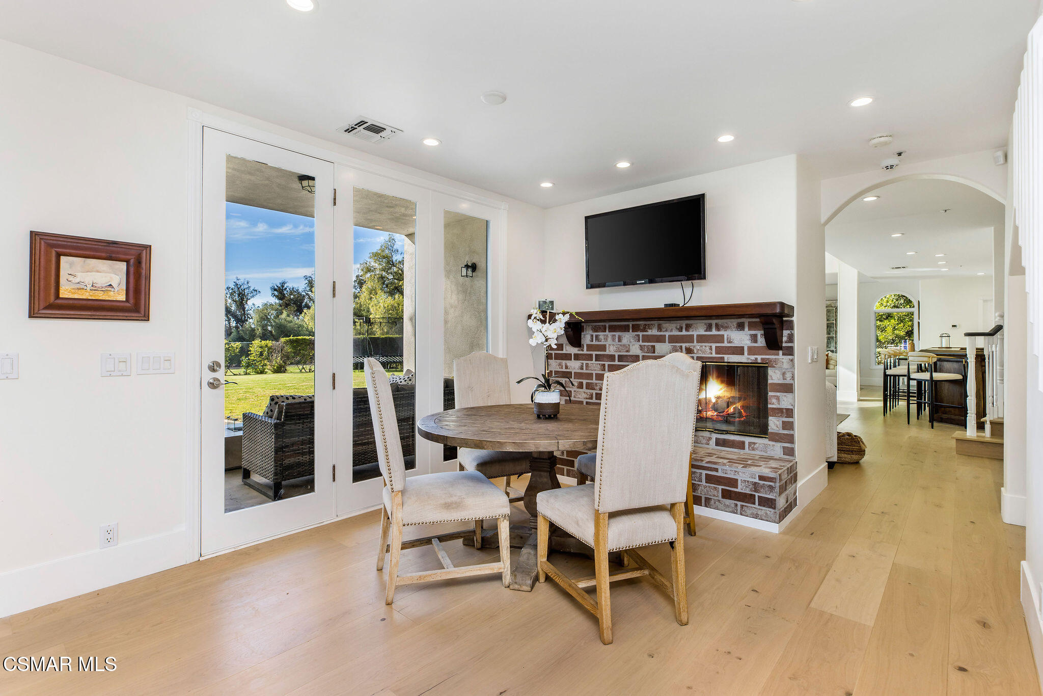 Dining area with a round table beside a brick fireplace and French doors opening to the garden.