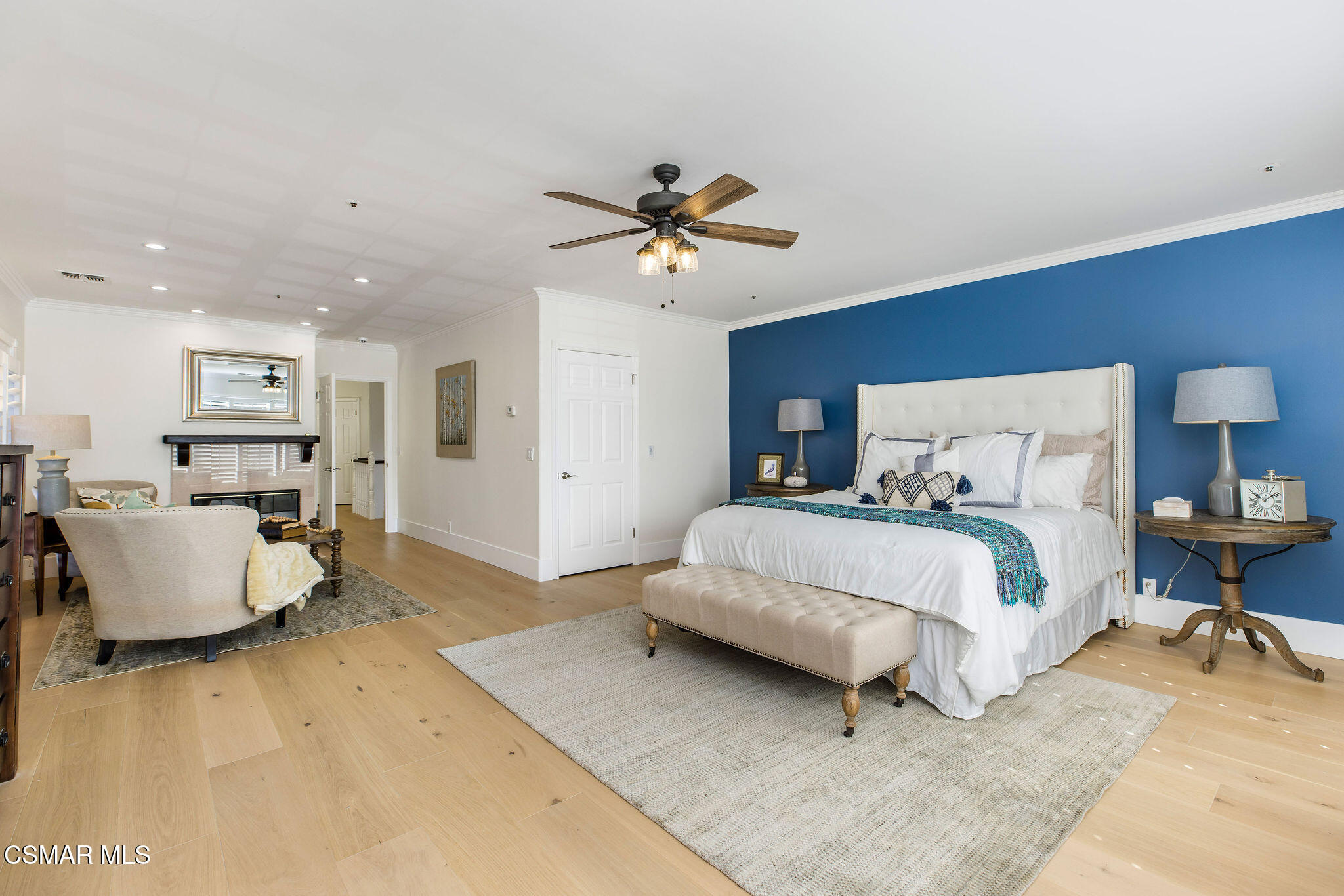 Staged bedroom with a white bed against a blue accent wall and an adjoining sitting area.