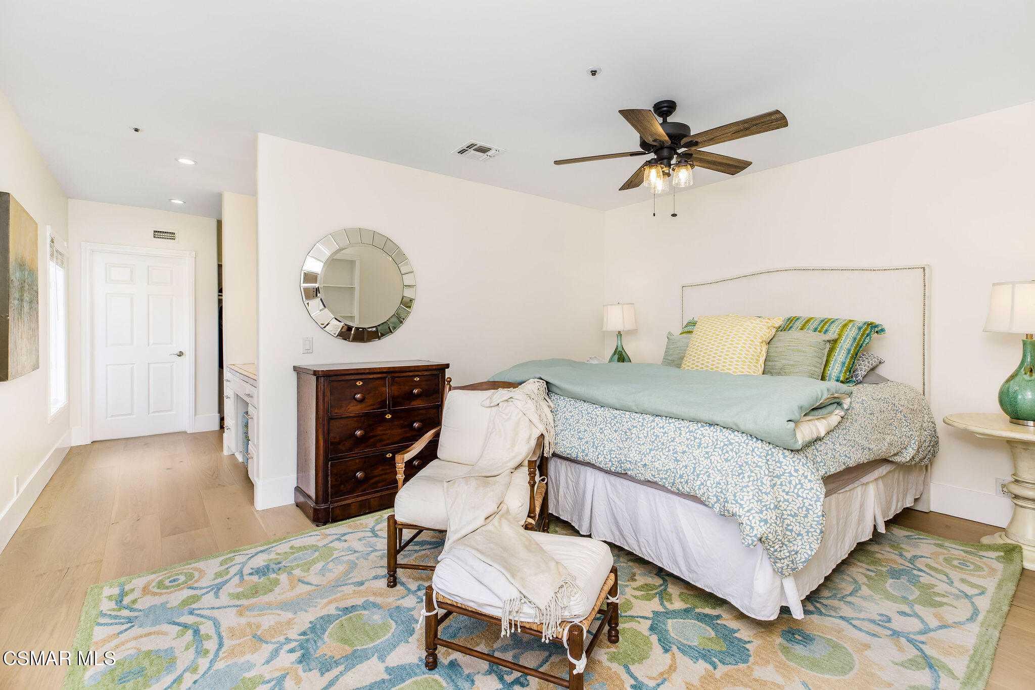 Bedroom with blue patterned bedding, a dark wood dresser, and a round mirror.