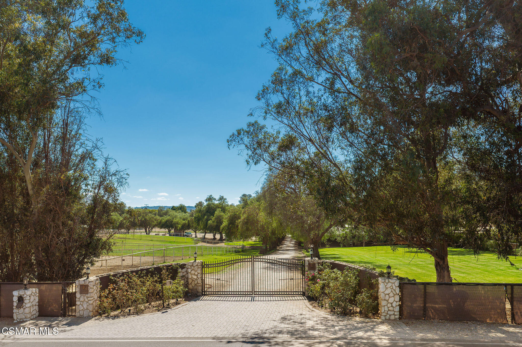 Gated property entrance with stone pillars and a tree-lined driveway.