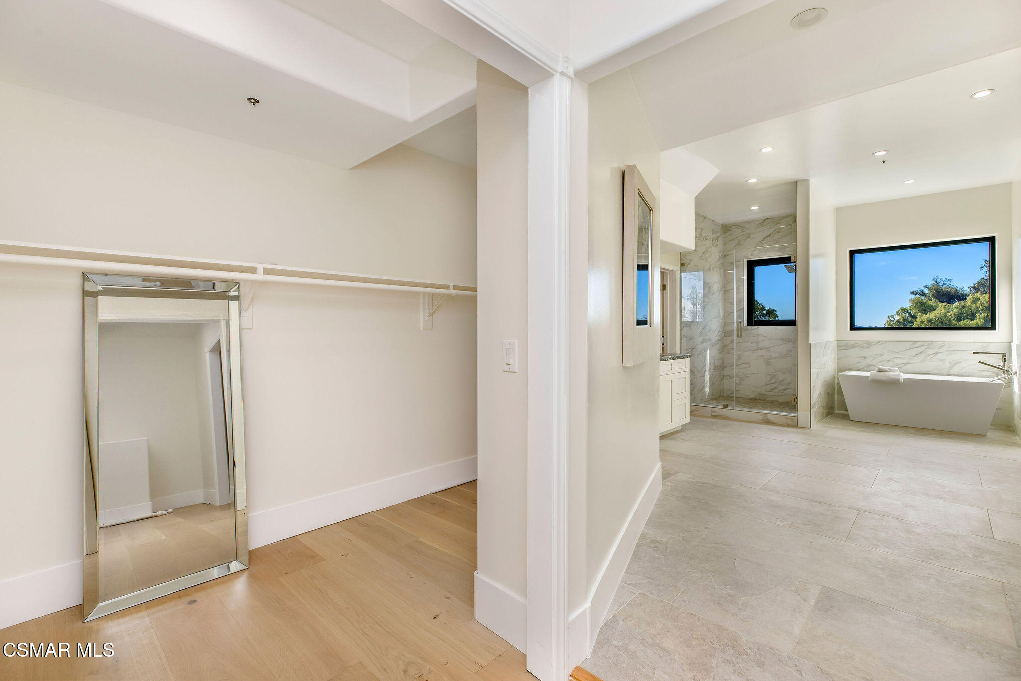 Primary bathroom with a freestanding tub, glass shower, and adjoining empty walk-in closet with a leaning mirror.