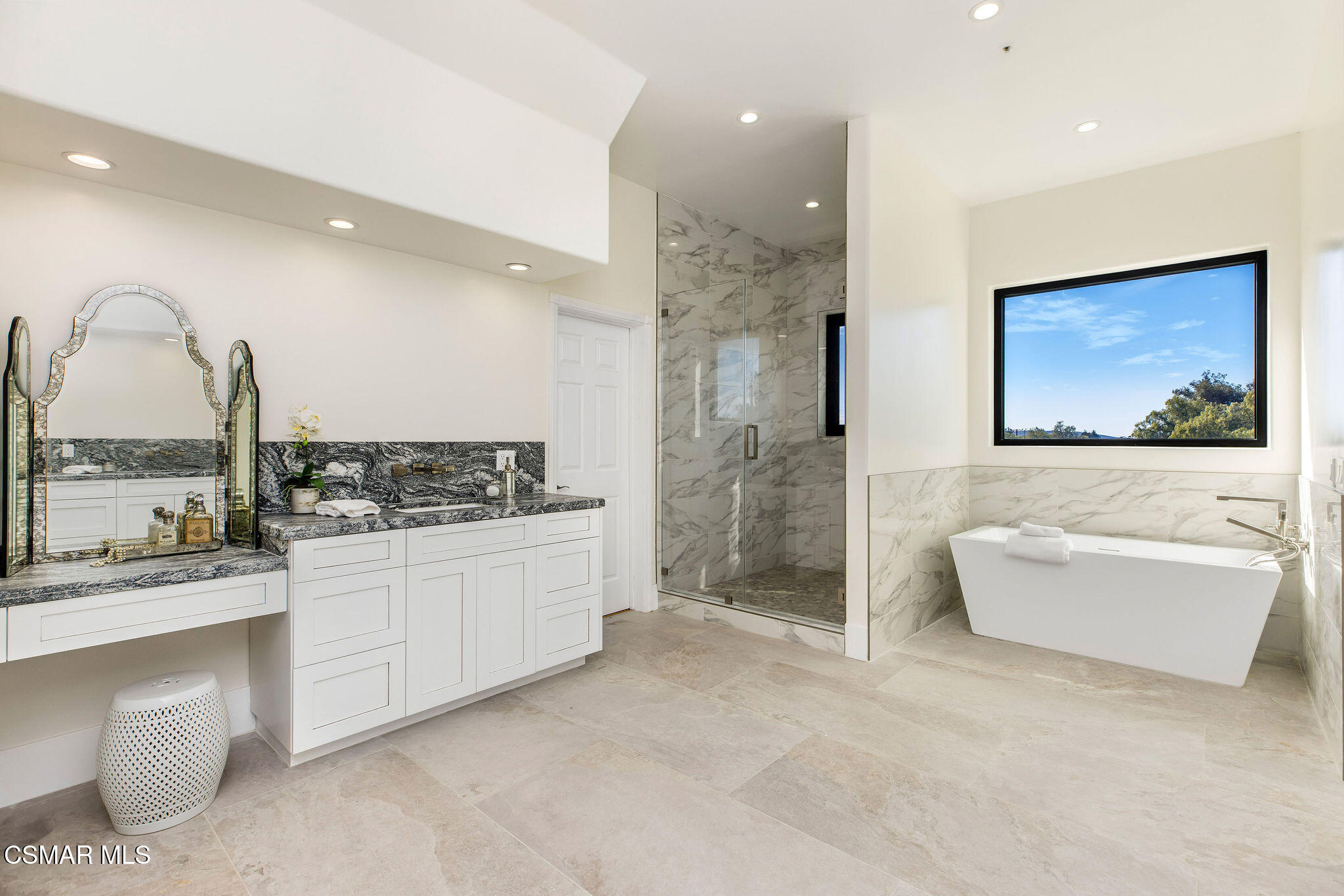 Bright bathroom with a marble shower, freestanding tub, and large window overlooking trees.