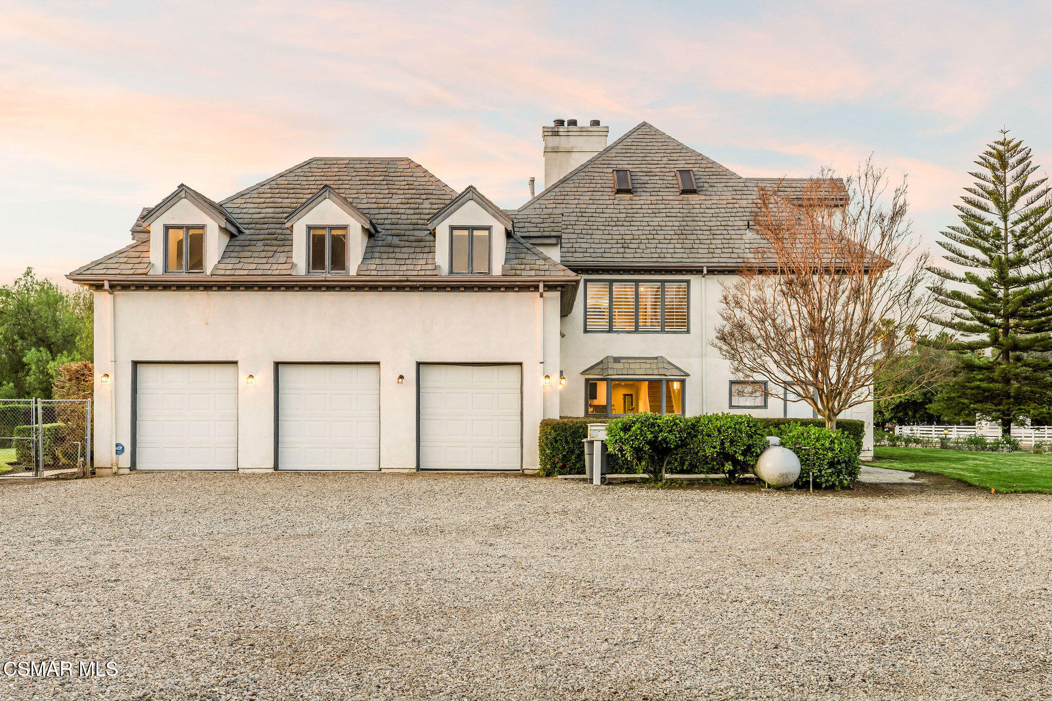 House exterior with three garage doors, a steep shingle roof, and a gravel driveway at dusk.
