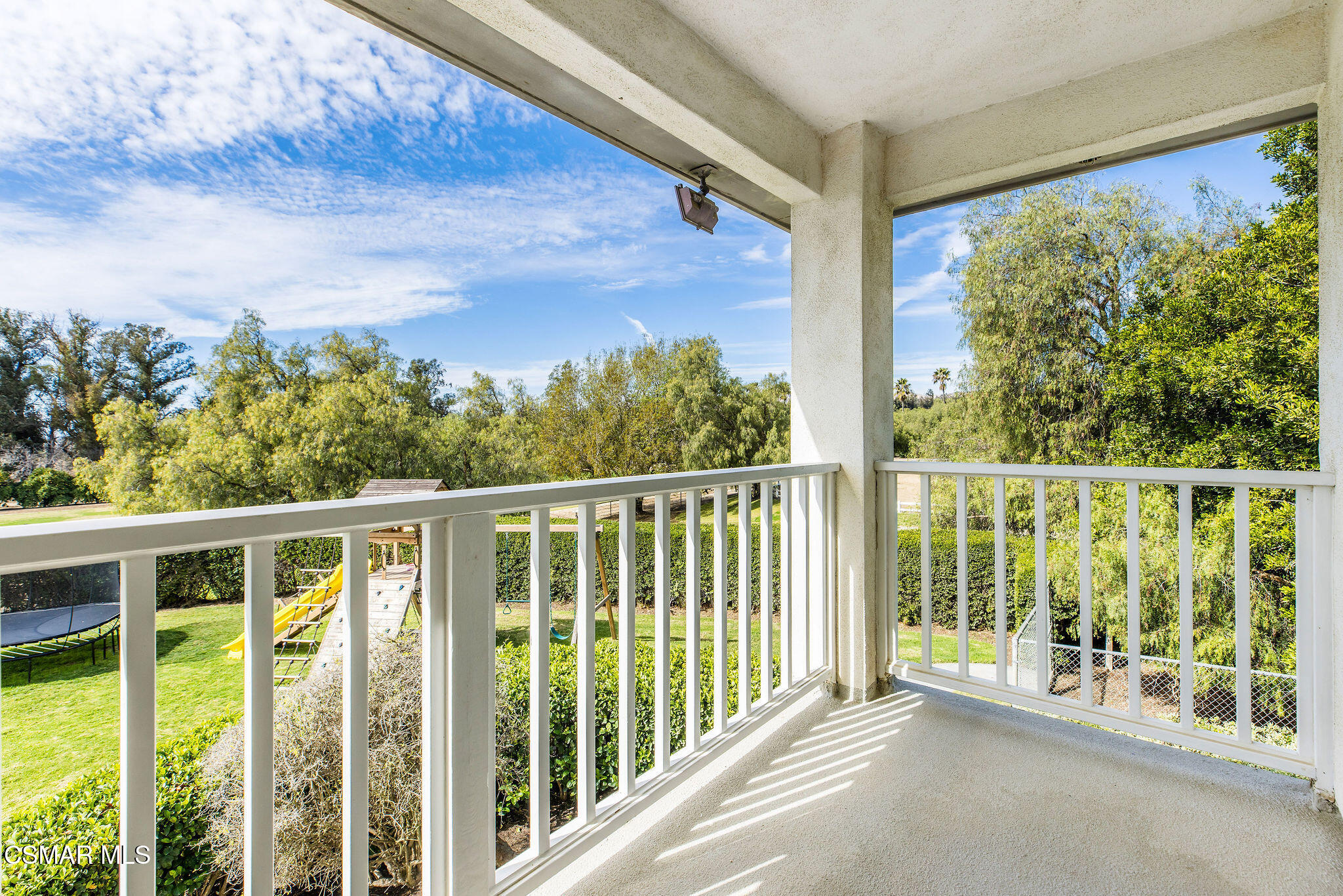 Covered balcony overlooking a tree-lined backyard with a trampoline and play equipment.