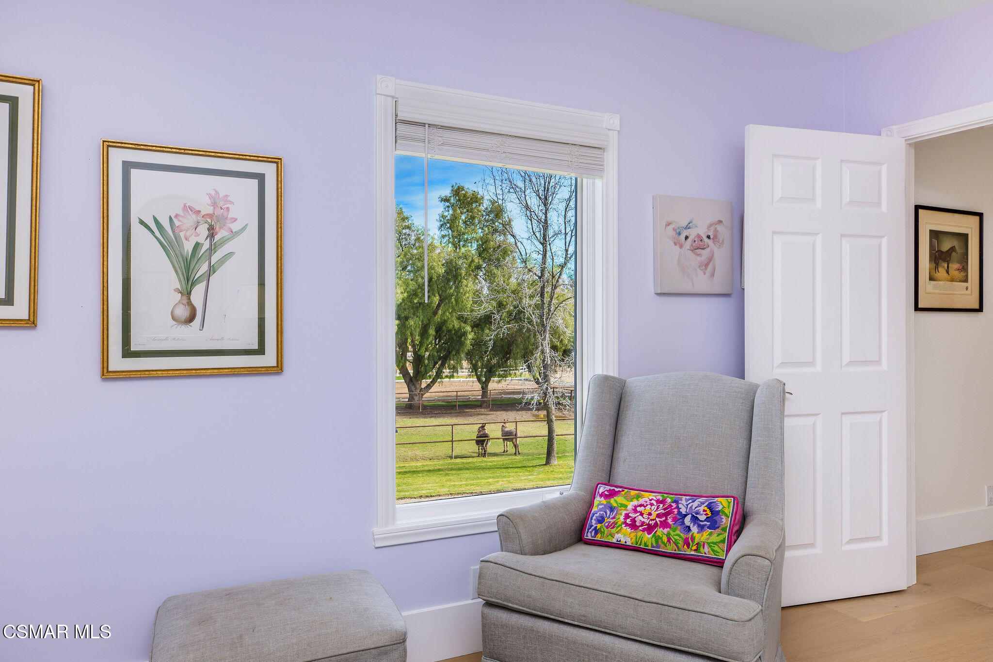 Furnished sitting area with a gray armchair and a window overlooking horses in a fenced pasture.