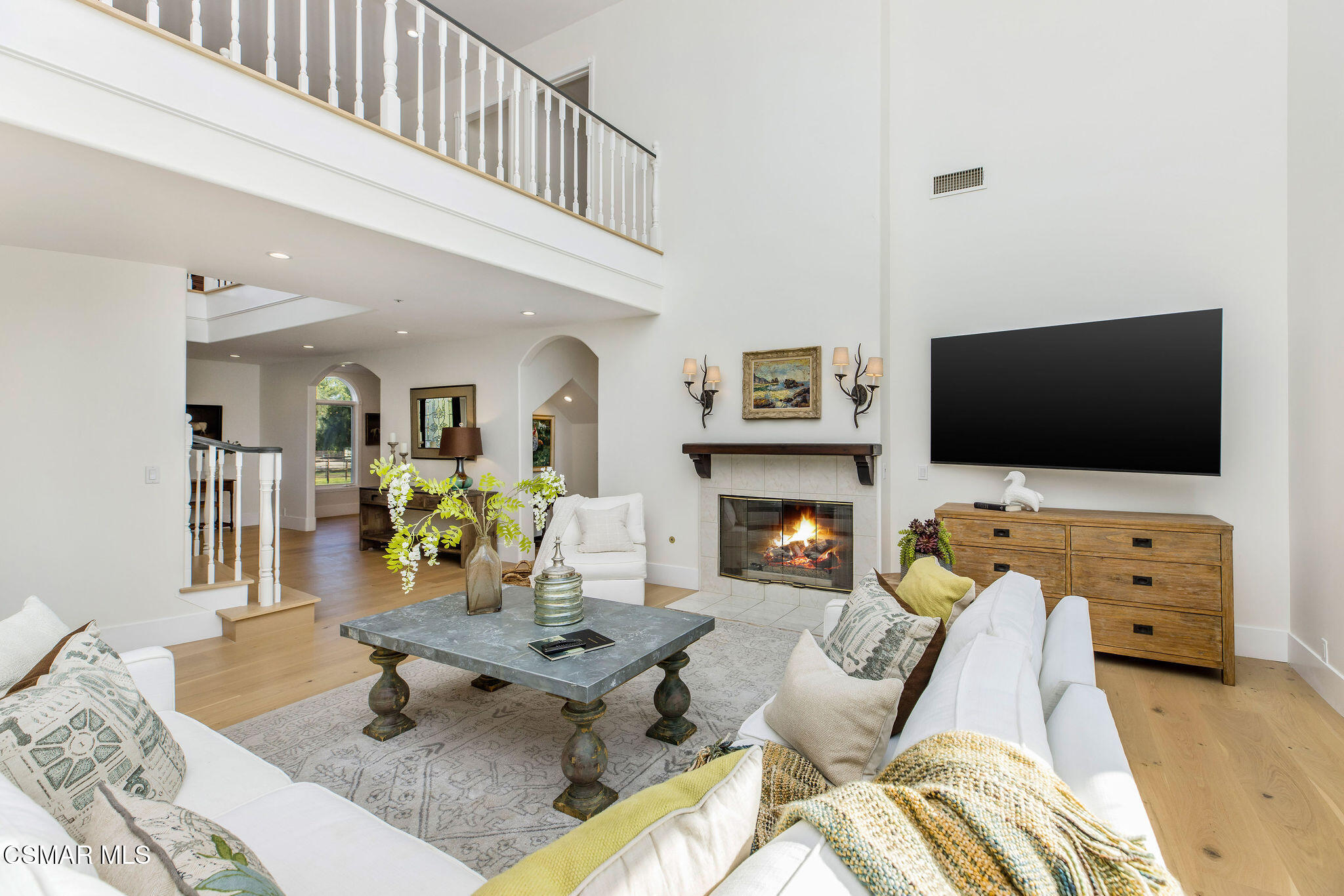 Staged living room with a tall open ceiling, fireplace, and upstairs balcony railing.