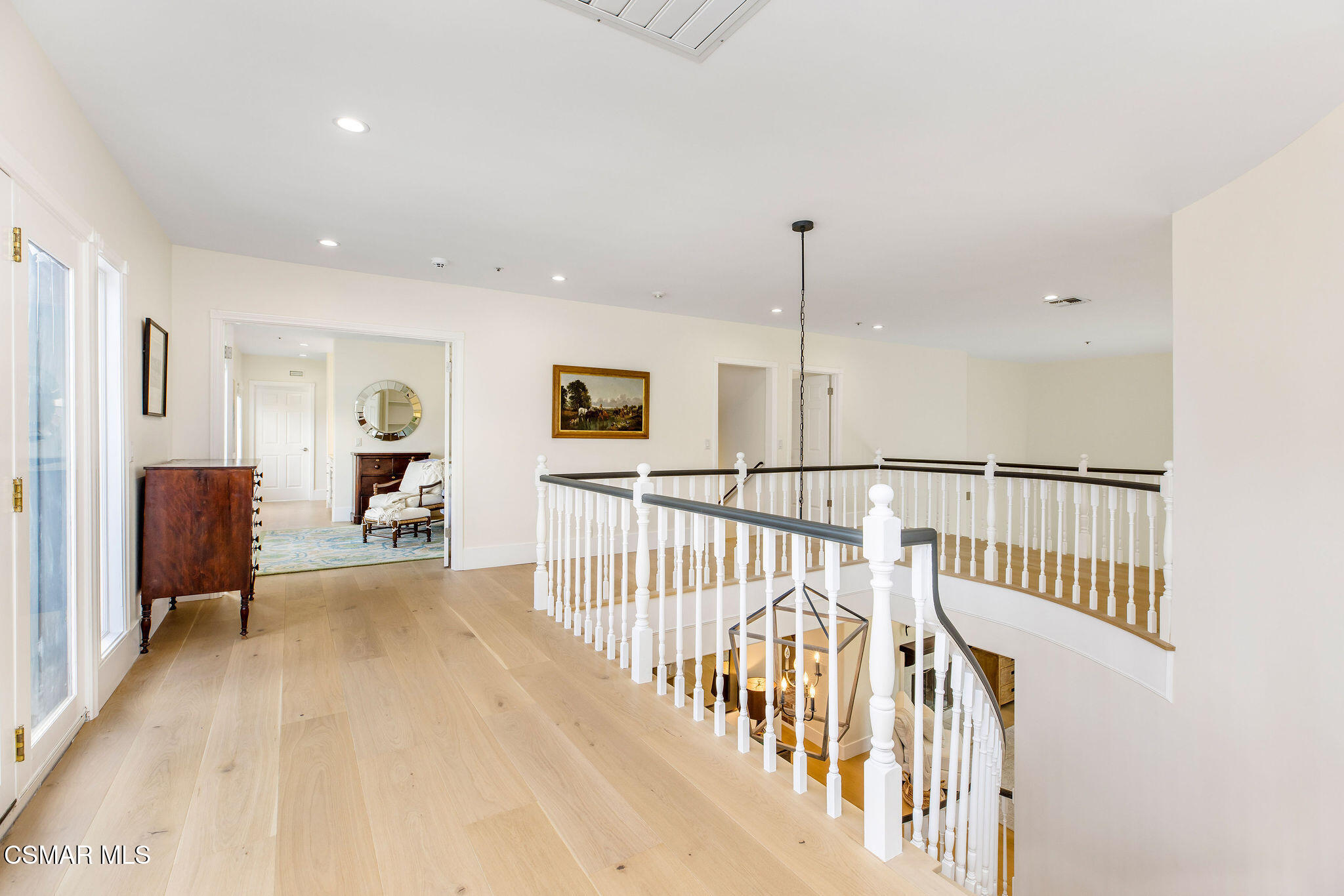 Upstairs landing with pale wood floors, tall windows, white railings, and an open staircase.