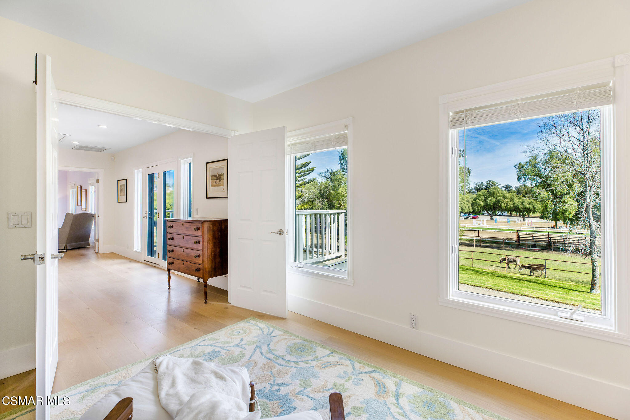 Bright sitting room with large windows overlooking a fenced pasture where horses graze.